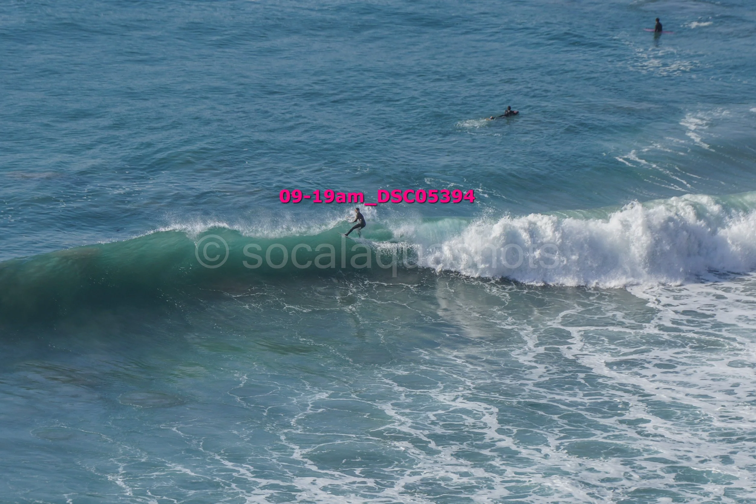 A person surfing on a wave in the ocean with two other surfers visible in the background.