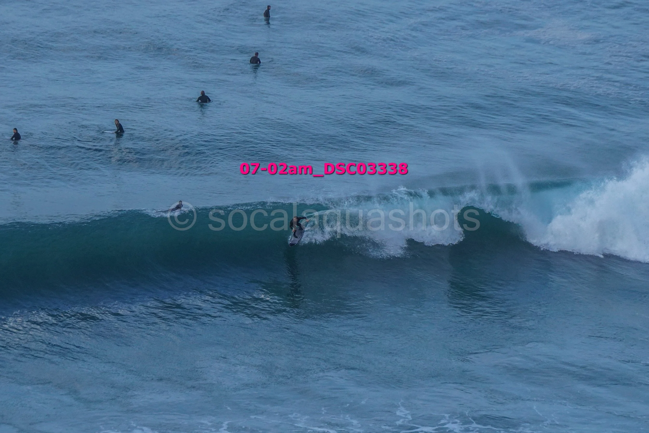 A person surfing on a wave with several people swimming in the background in the ocean.