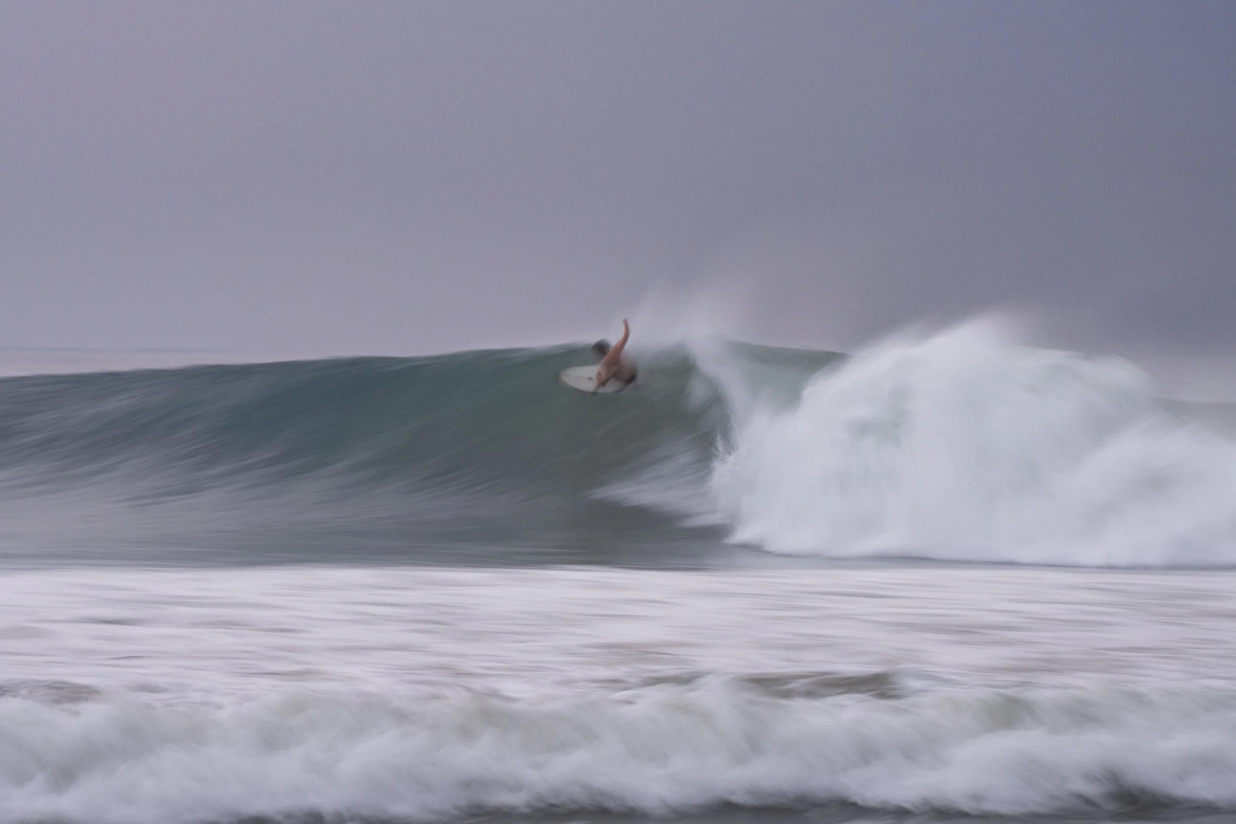 Surfer riding a wave in rough ocean waters under gray sky.