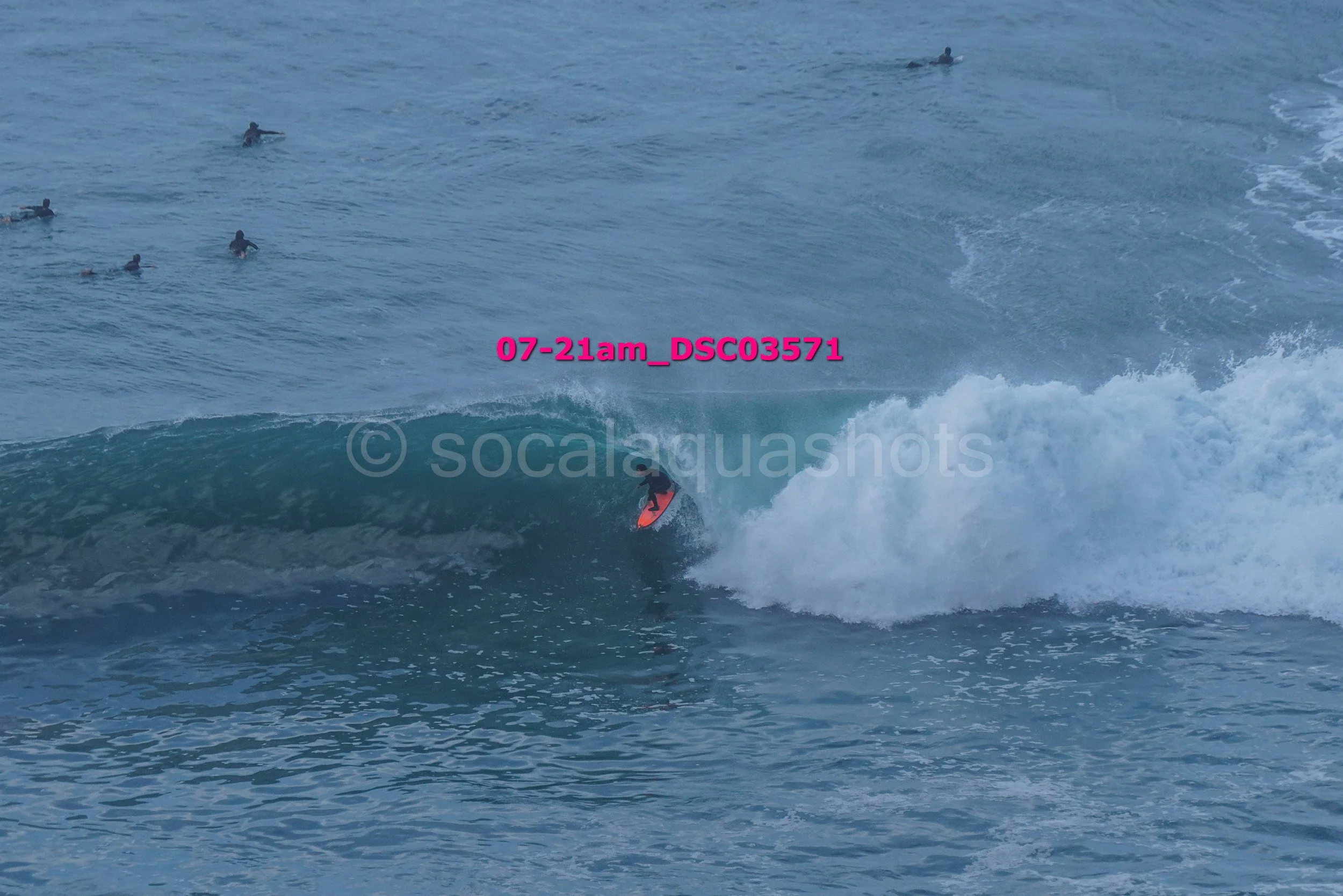 A person surfing on a wave in the ocean with other surfers in the background.