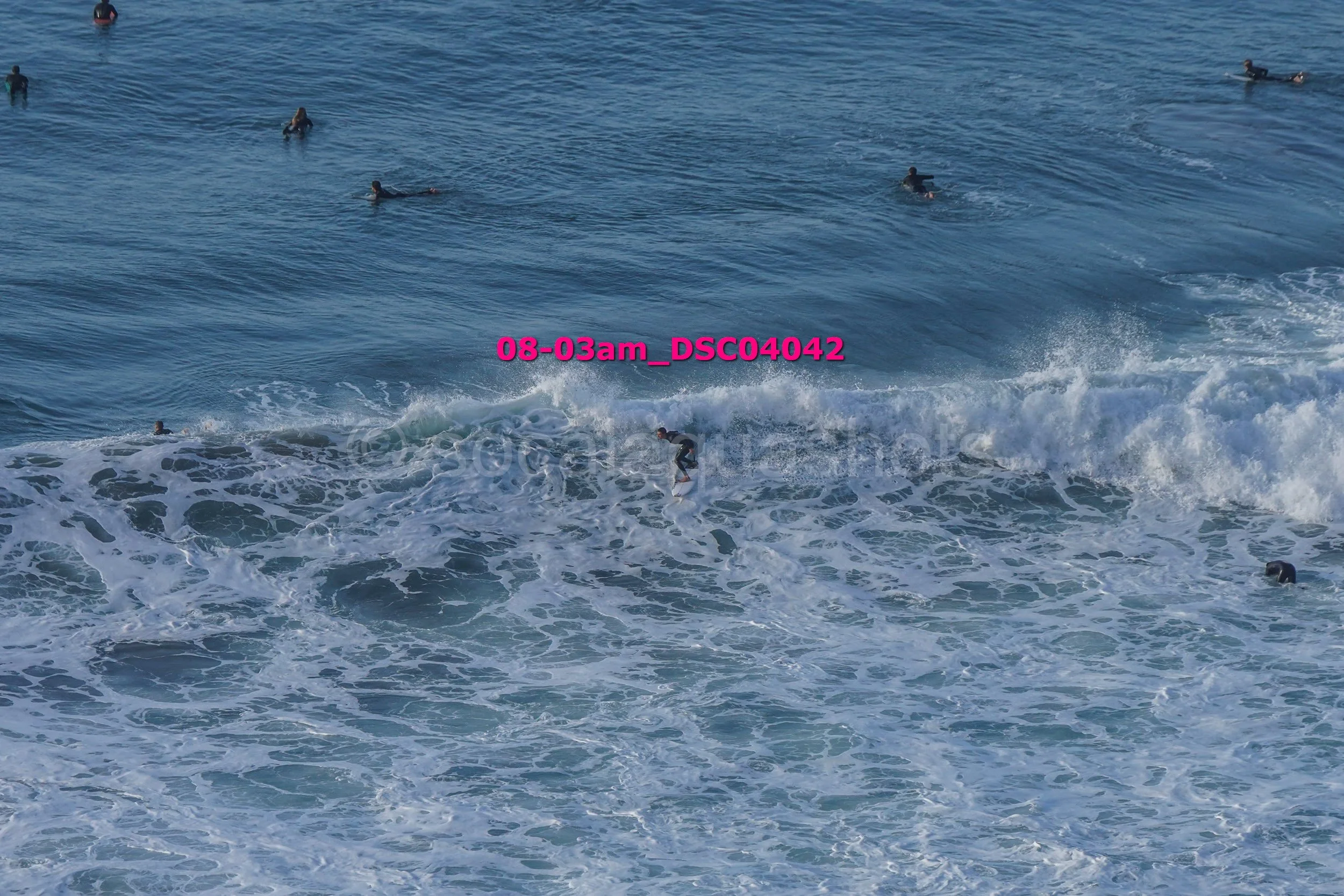 Surfer riding a wave with several people swimming in the ocean in the background.