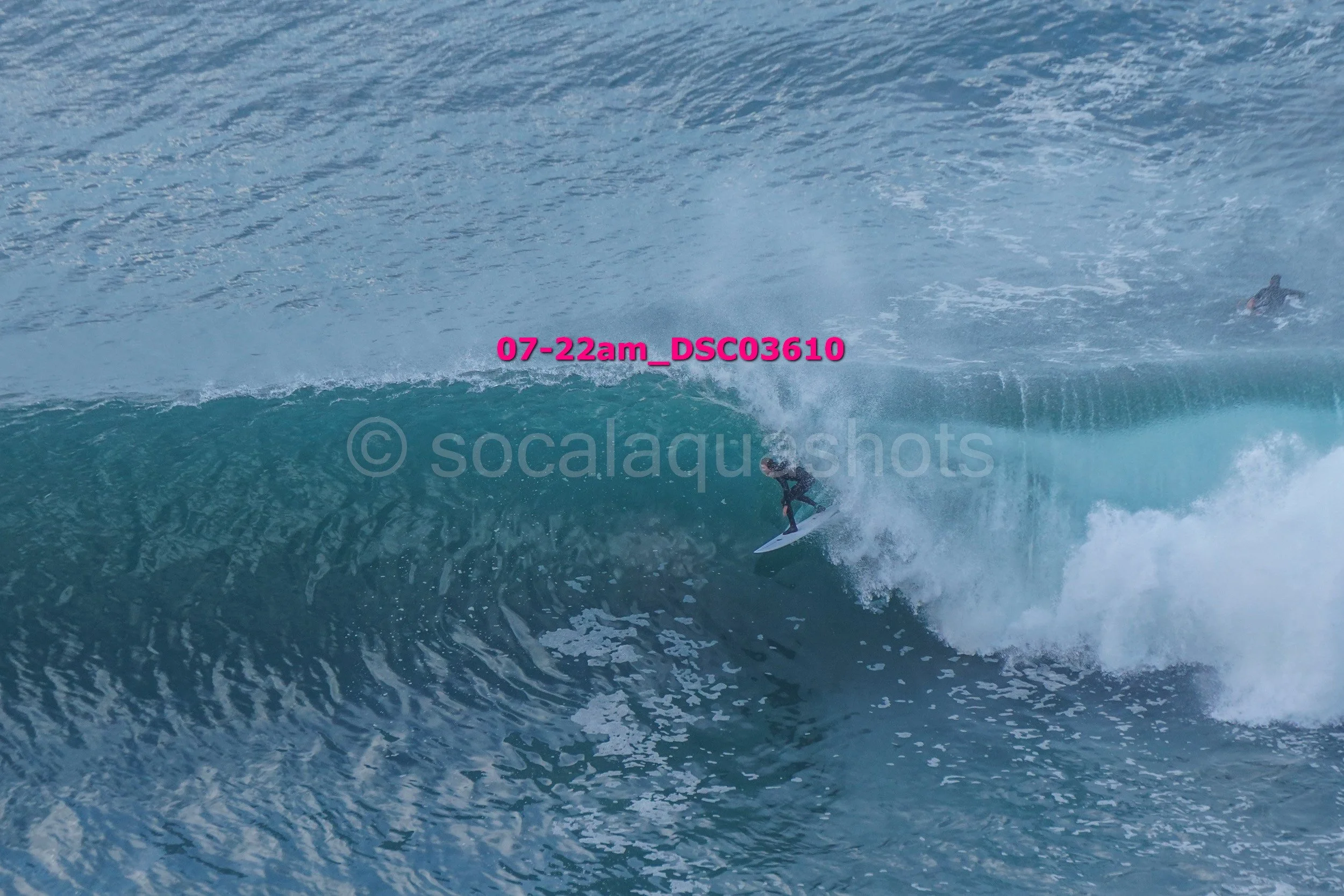 Surfer riding inside the wave, with another surfer visible further back in the water.