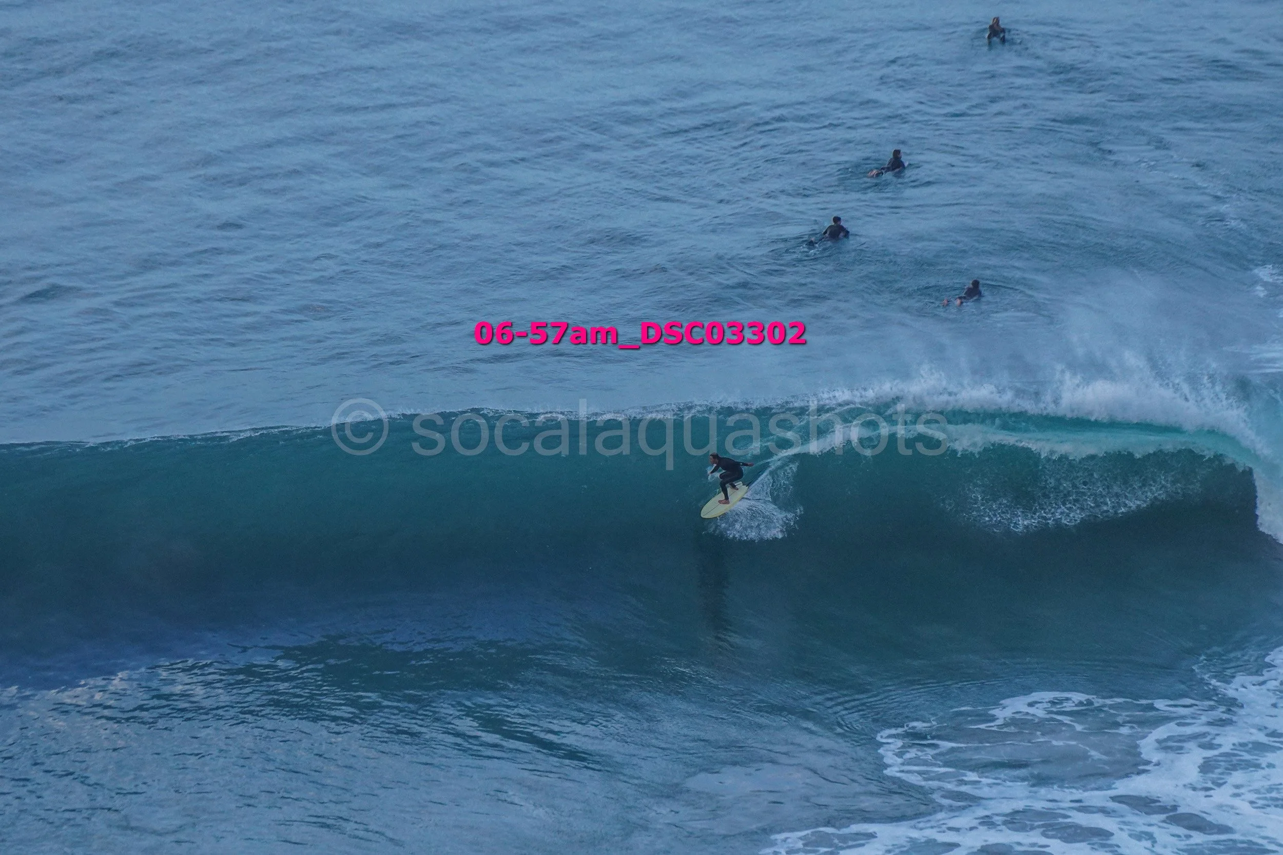 A person surfing on a wave with several people swimming in the ocean in the background.