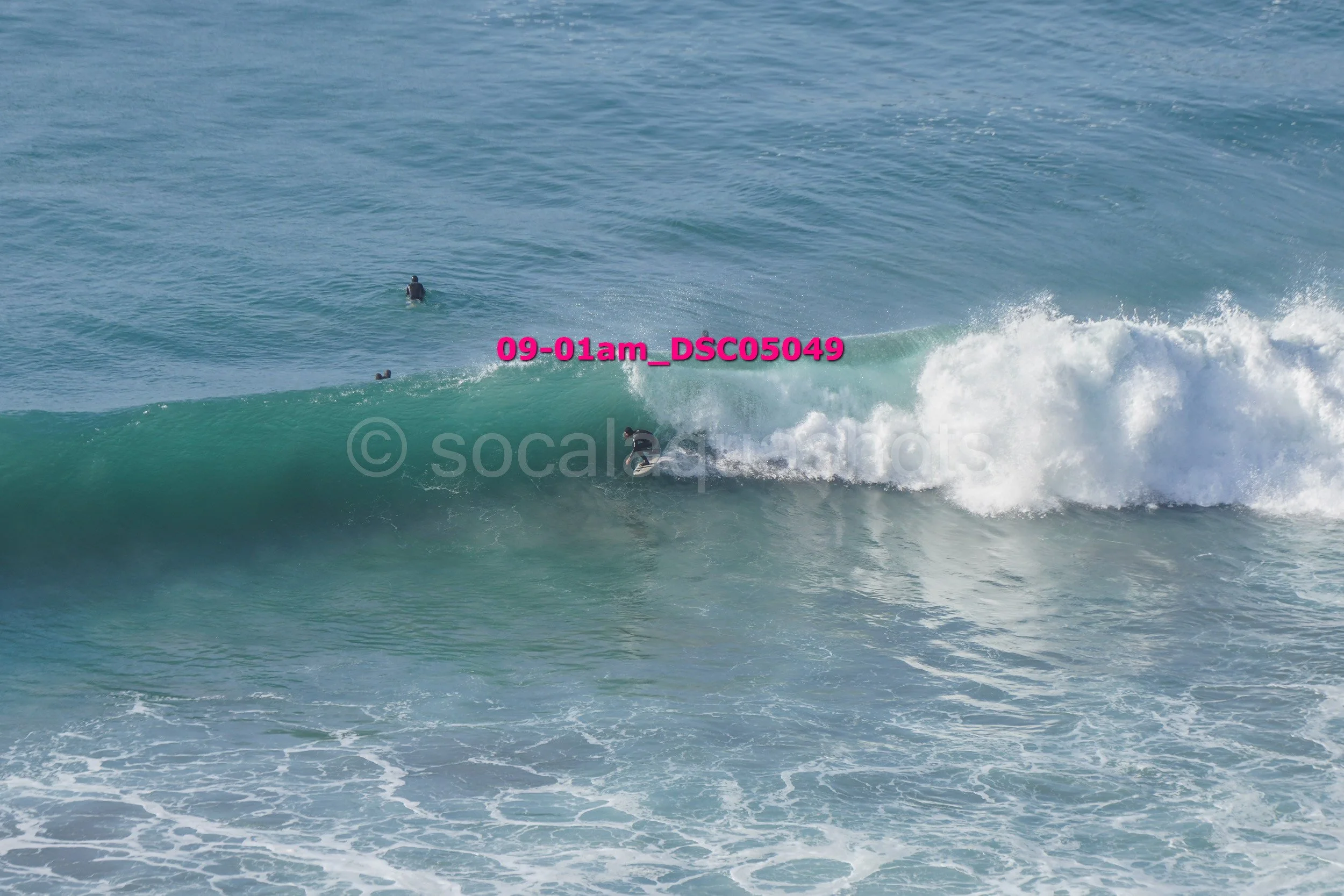 A surfer riding a wave in the ocean with two other surfers in the background.