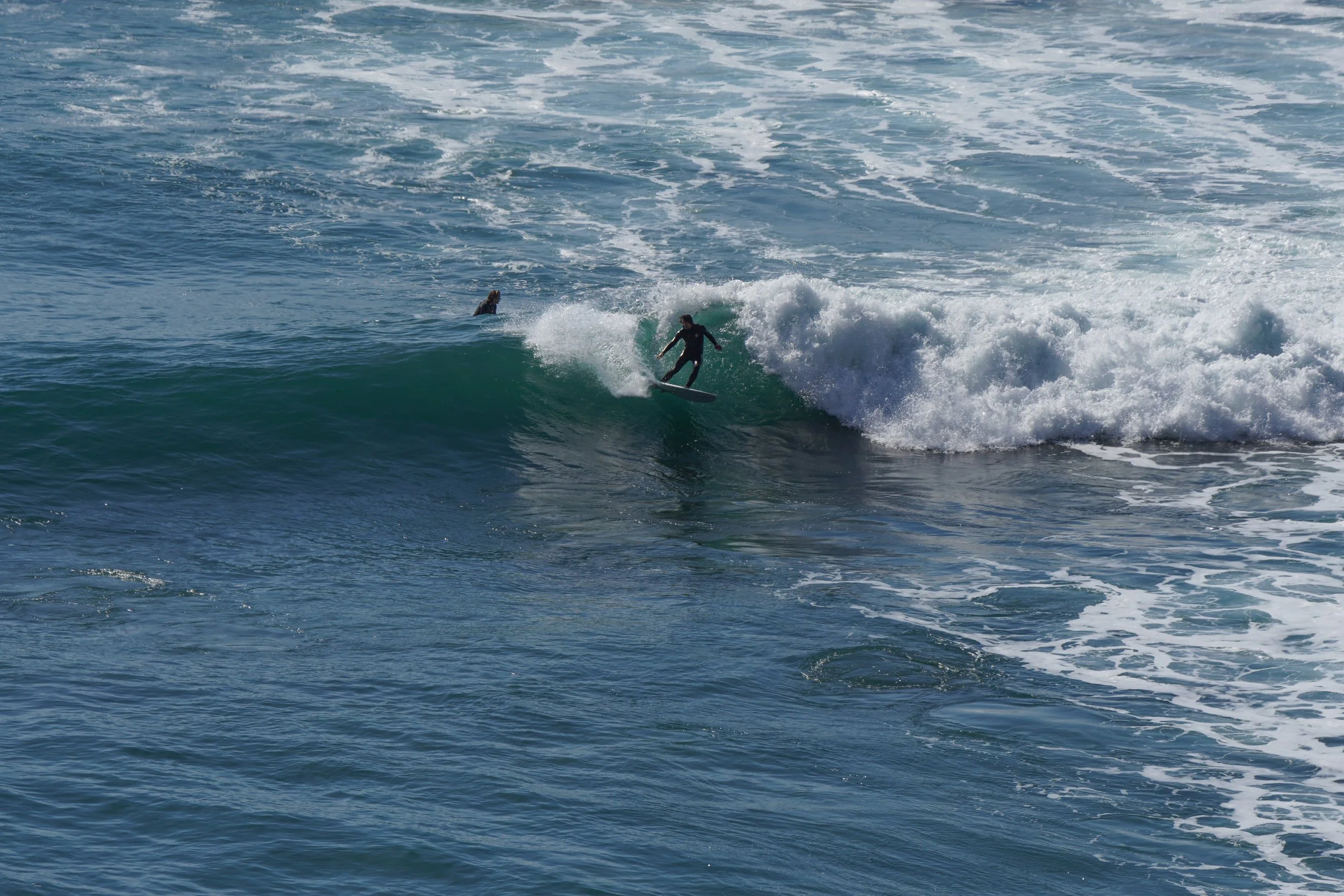 A person surfing on a wave in the ocean with another person in the water nearby.