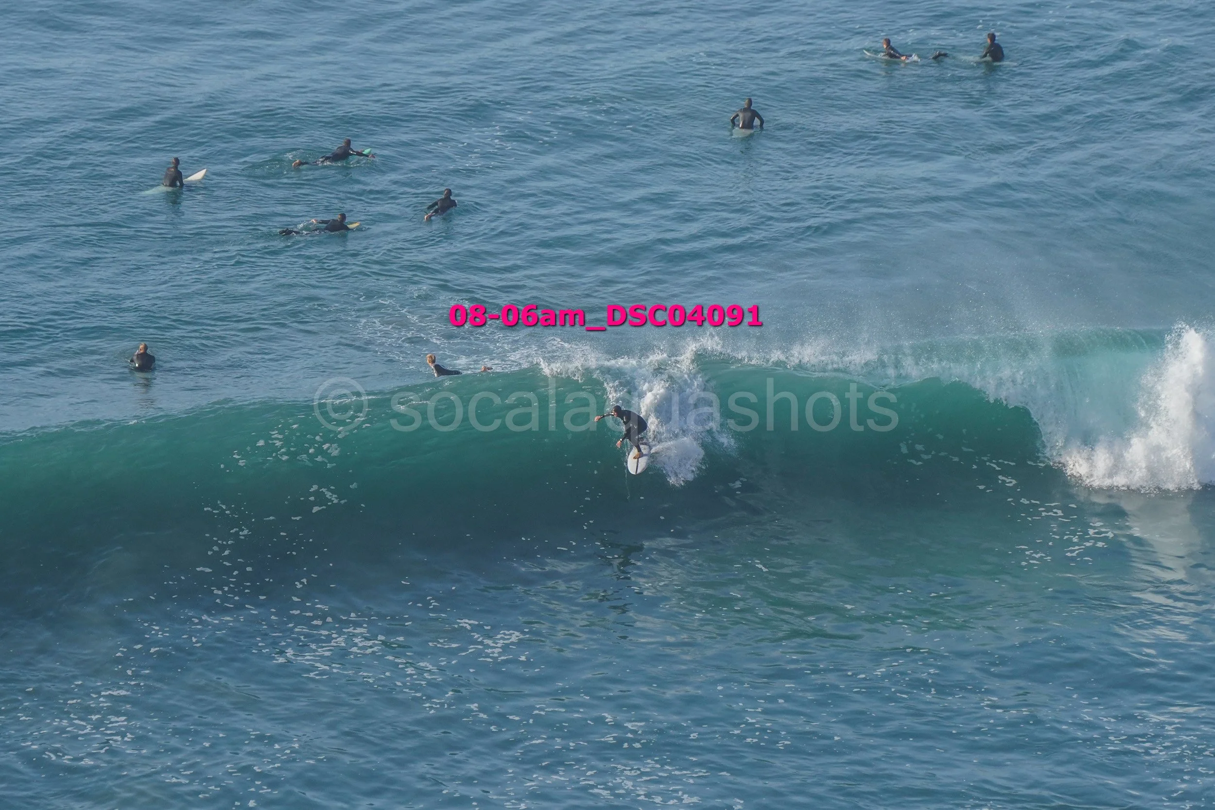 A group of surfers in black wetsuits riding and observing waves in the ocean.