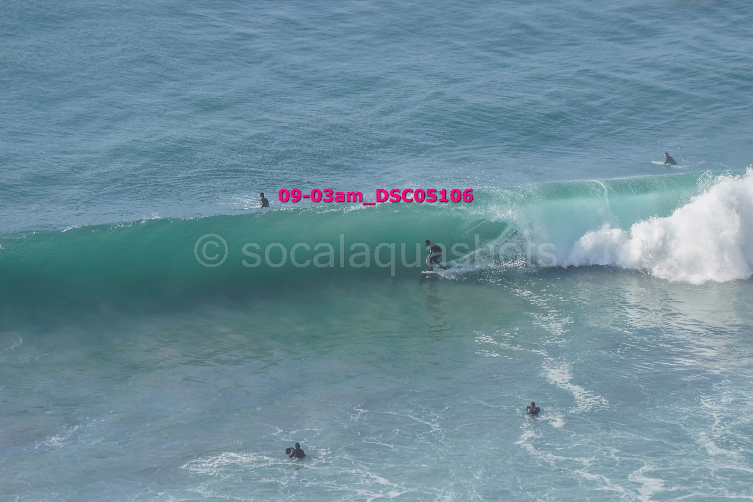 Surfer riding a wave with several other surfers watching in the water.