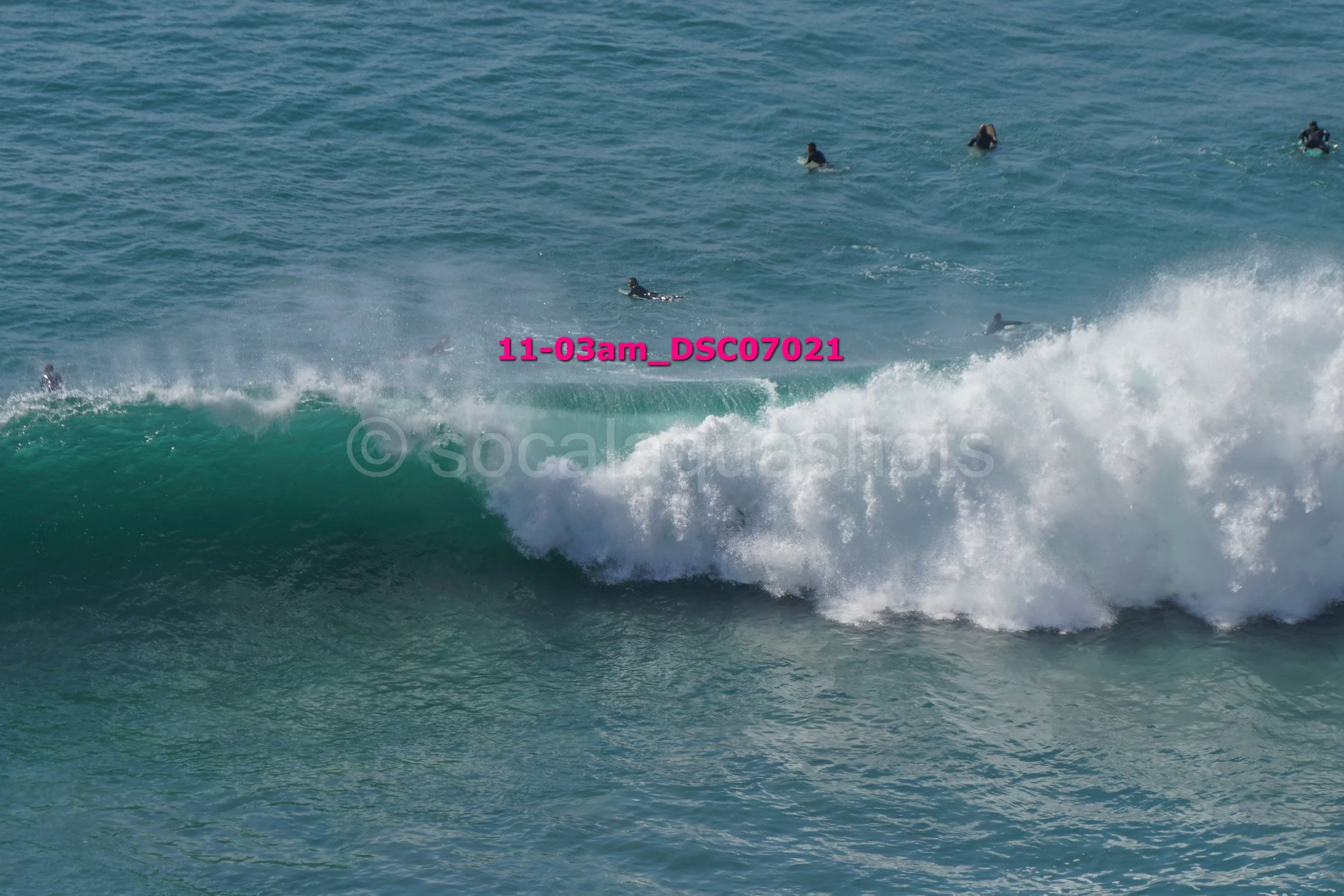 Scene of surfers riding a wave in the ocean with several surfers in the background.