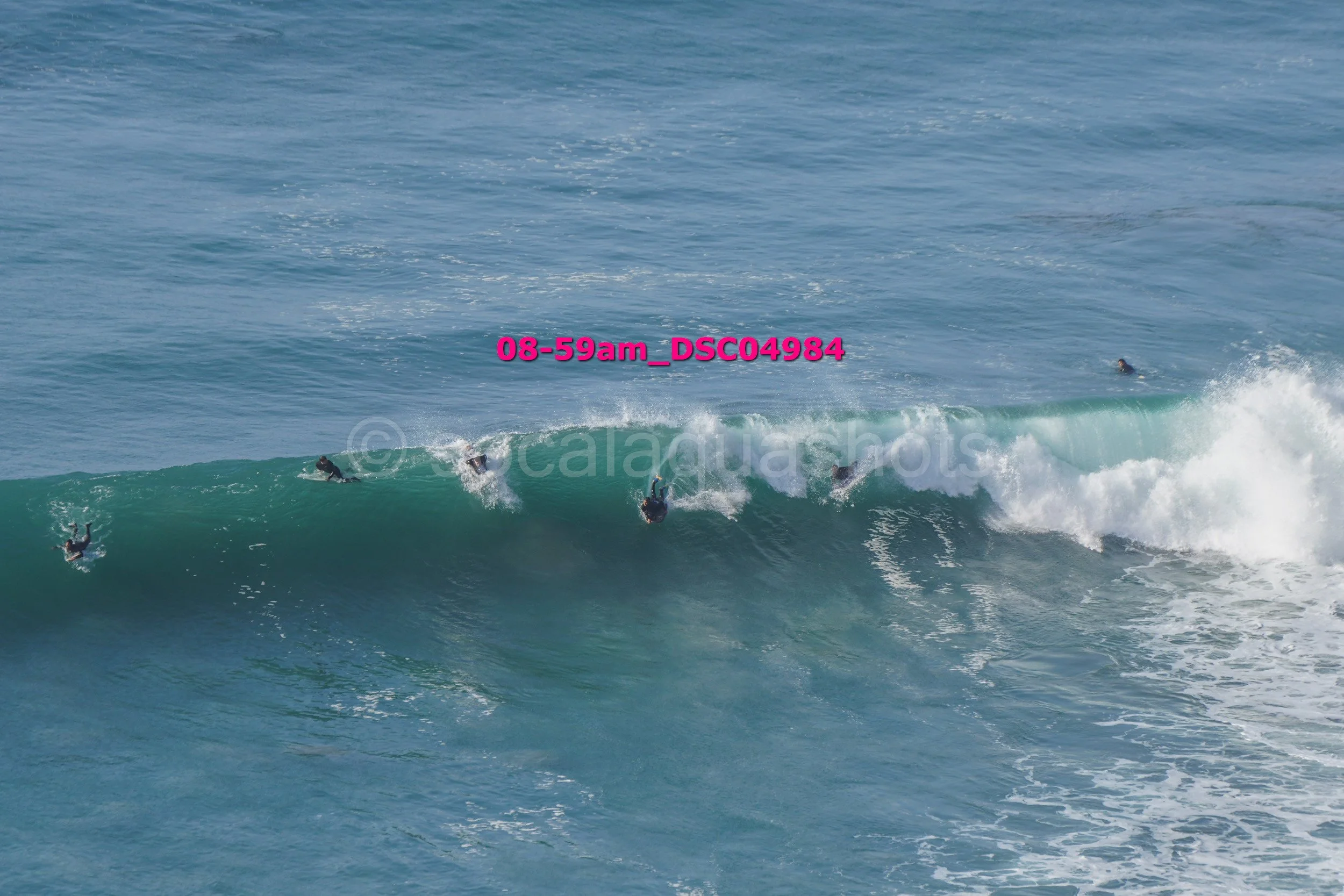 Multiple surfers riding a large ocean wave, some falling into the water.