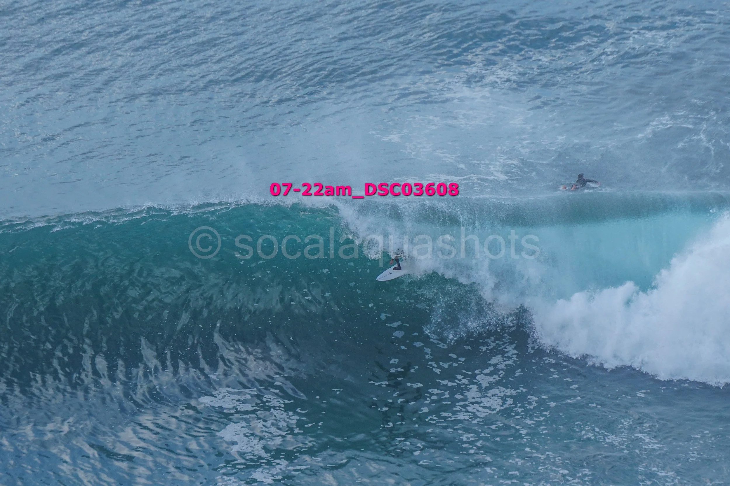 A person surfing on a large ocean wave during daytime with calm water in the background.