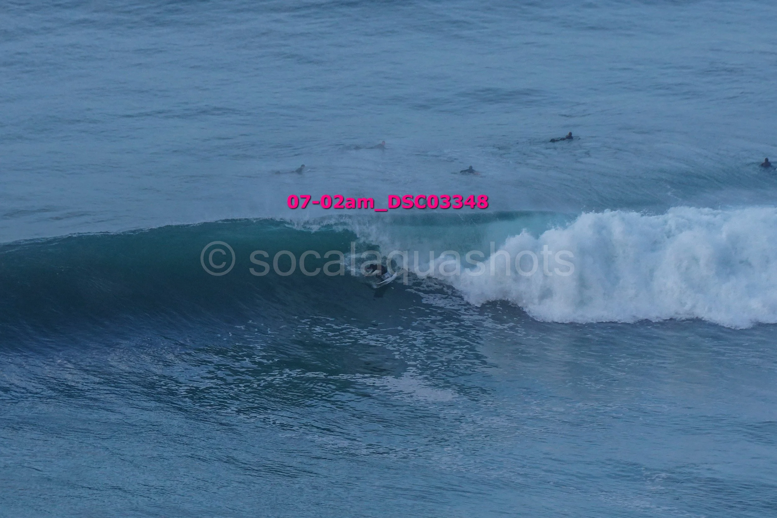 Surfer riding a wave in the ocean with several other surfers in the water nearby.