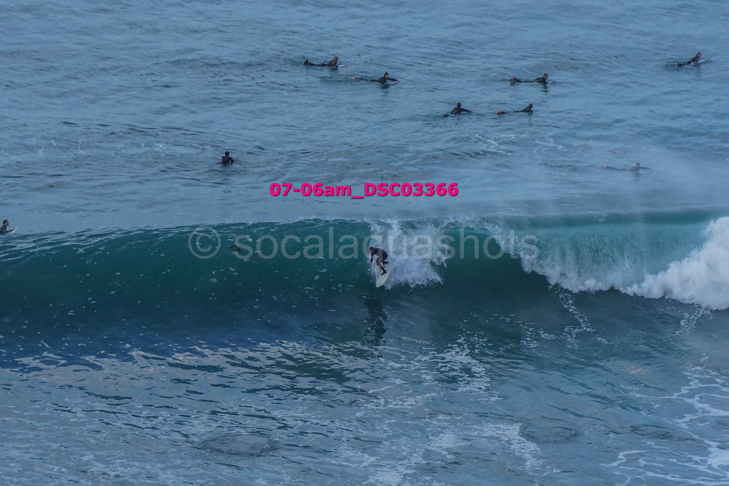 A person surfing on a wave with many people in the water watching from a distance.