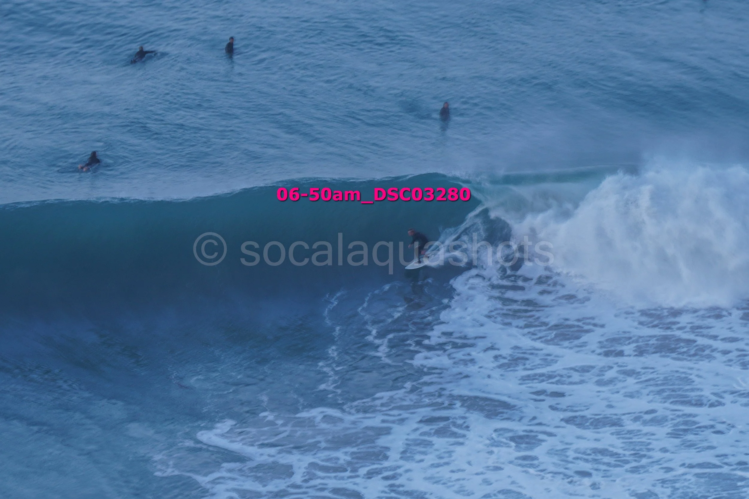 Surfer riding a large wave with several surfers in the water in the background.