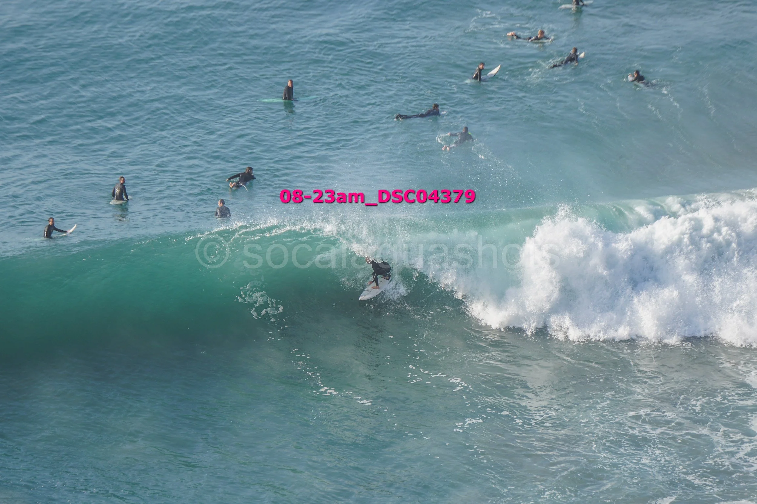 Surfer riding a large wave surrounded by multiple surfers in the water.