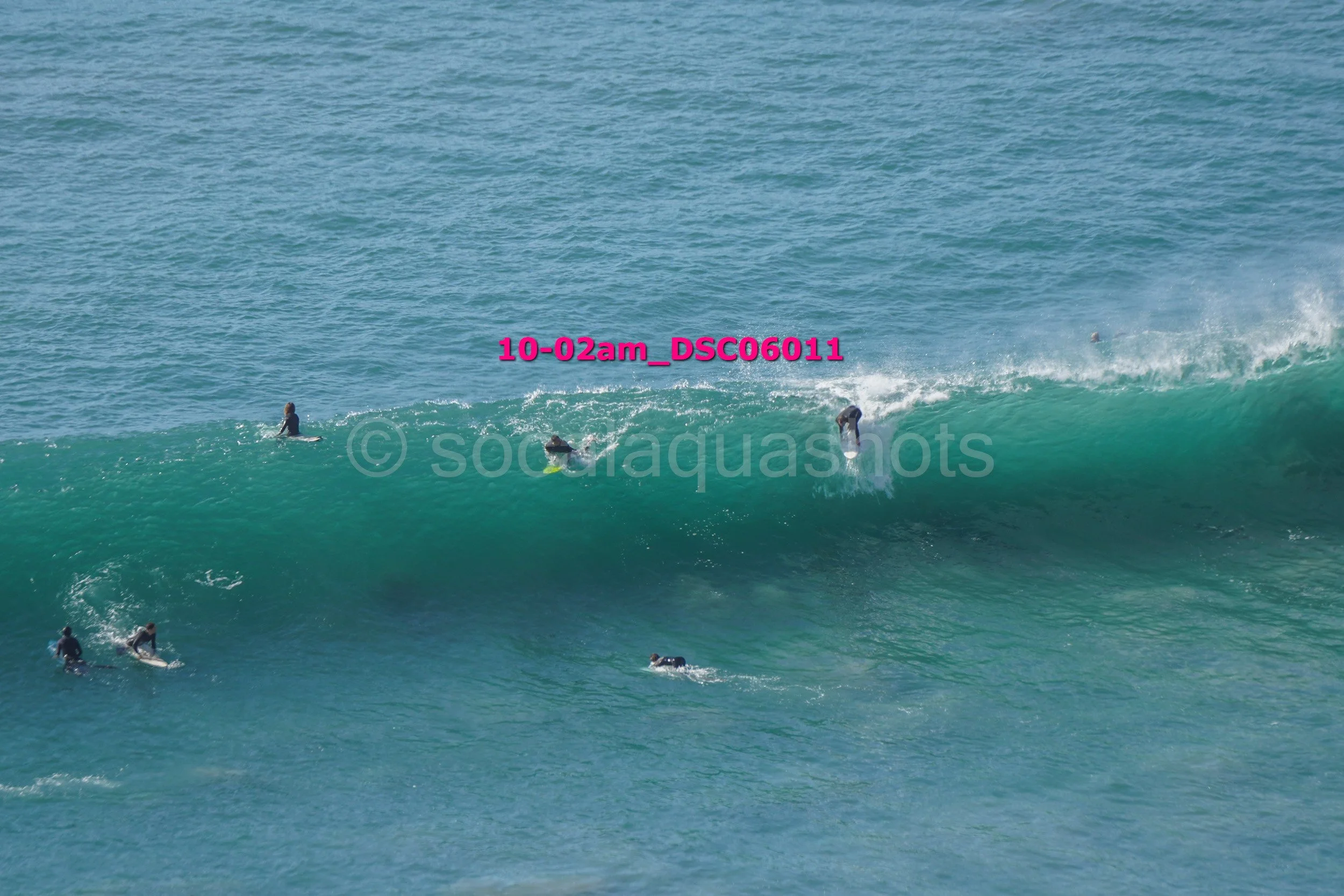 Surfers riding and waiting for waves in the ocean, with one person surfing on a breaking wave.