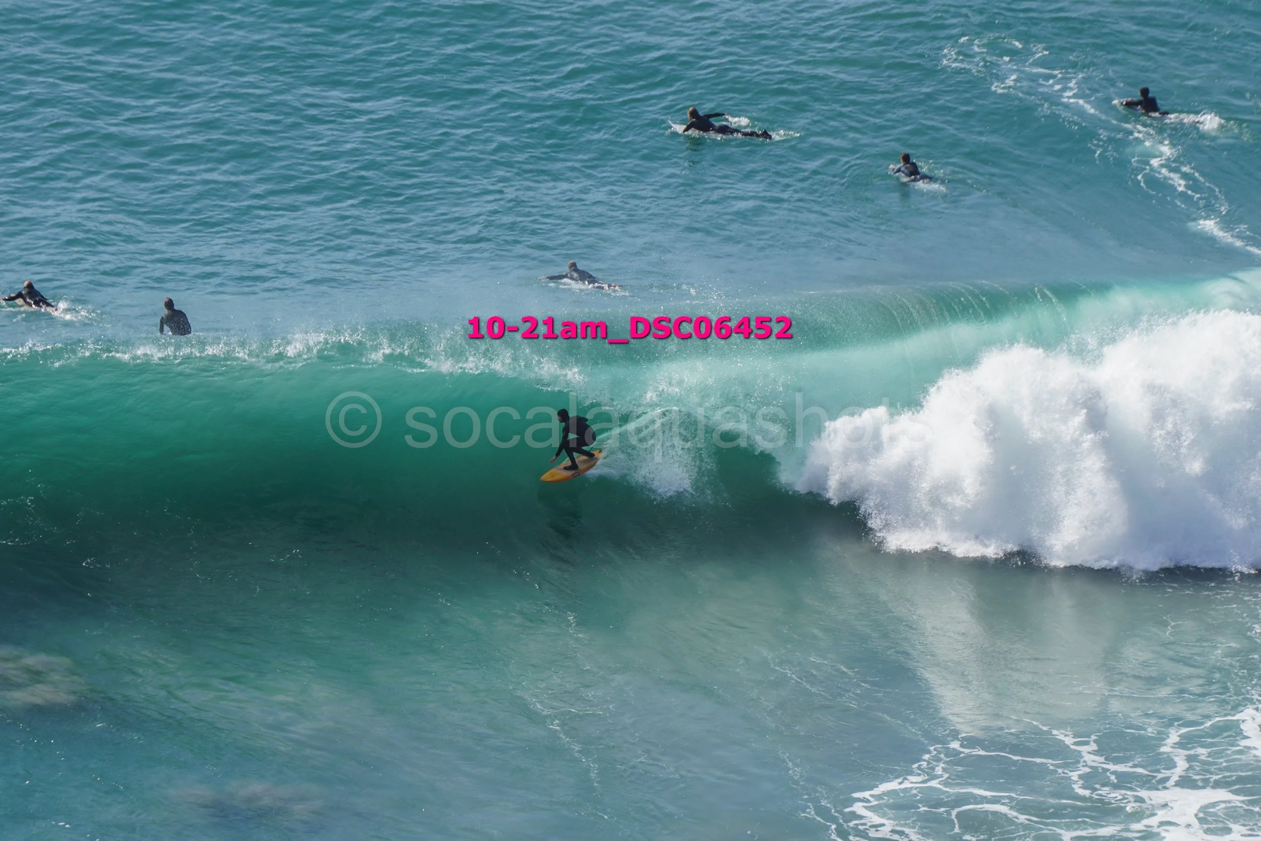 Surfer riding a wave with several people swimming or surfing in the background in the ocean.