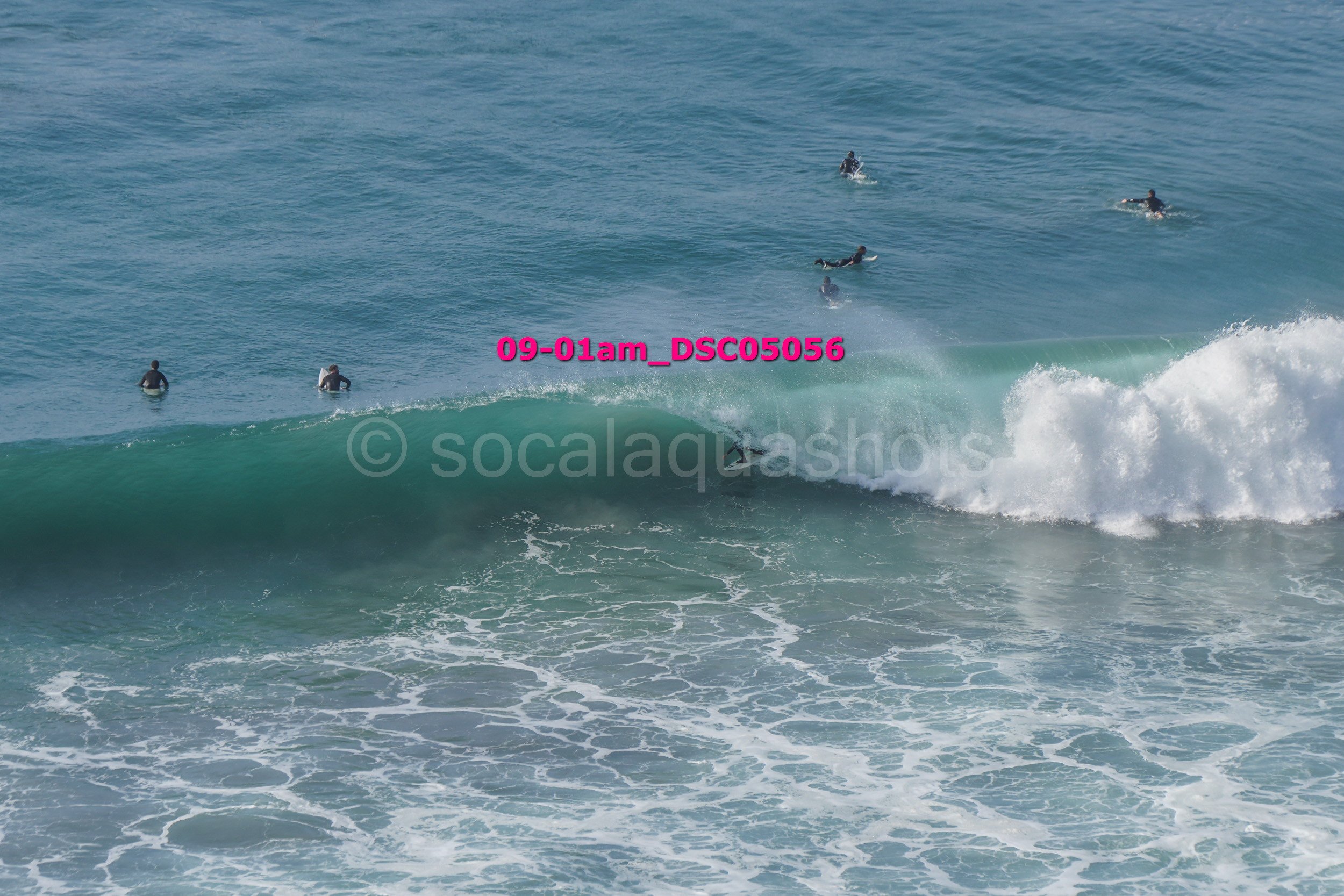 A person surfing on a wave with multiple surfers in the water around them.