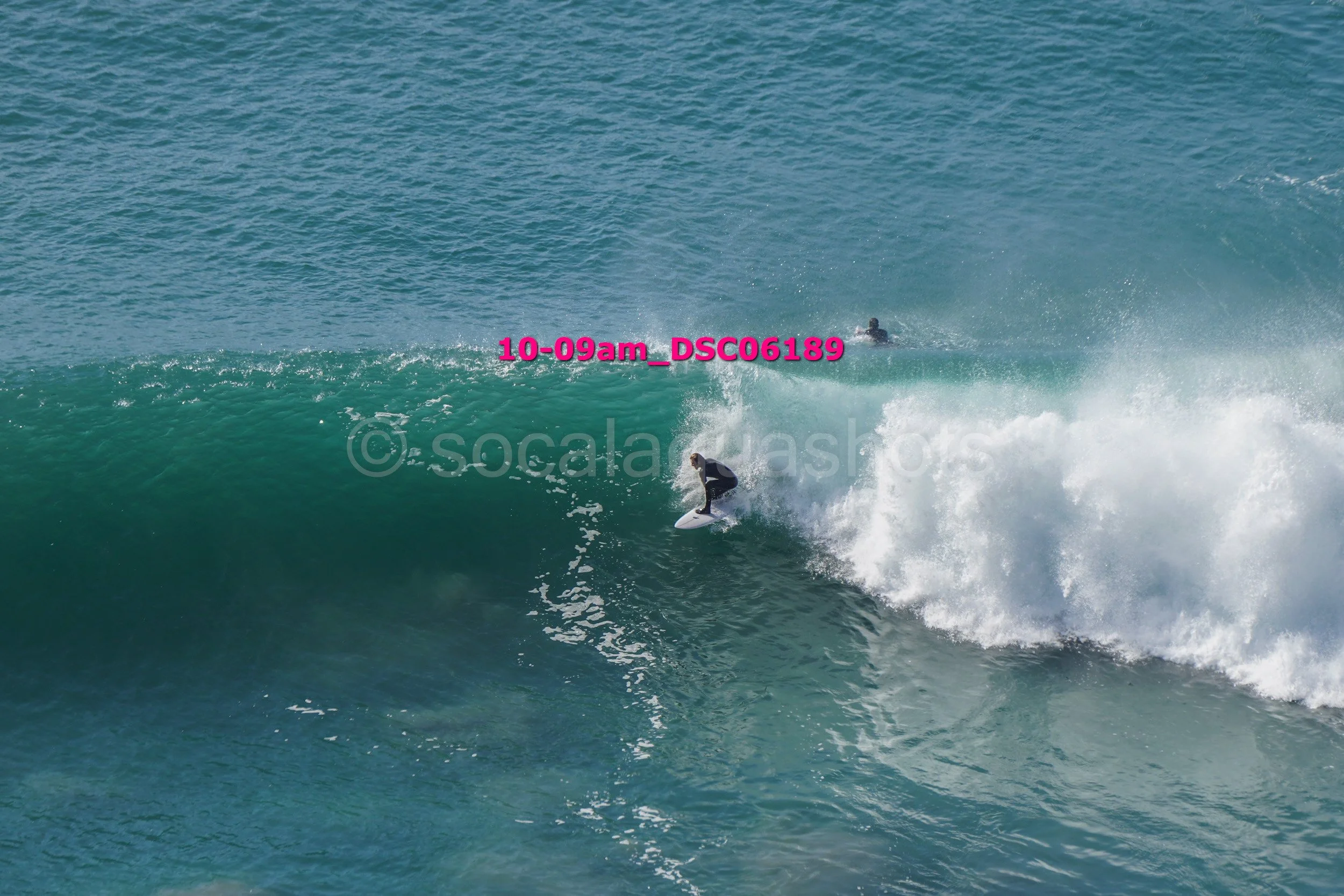 A person surfing on a large wave in the ocean with another surfer in the background.