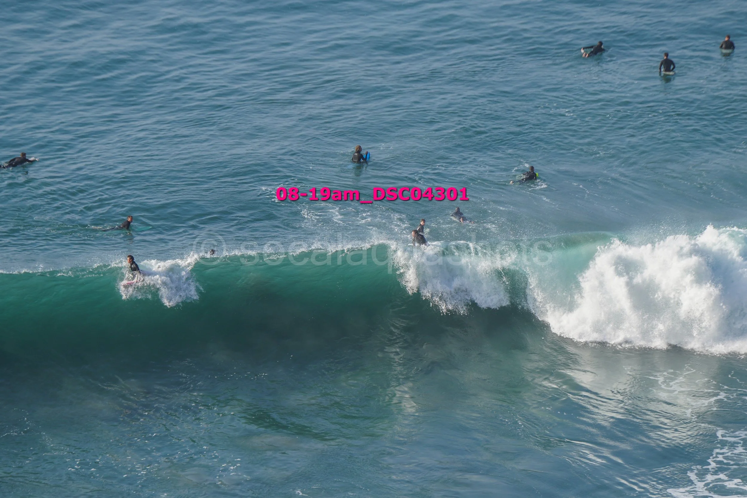 People surfing and swimming in the ocean with waves and clear blue water.