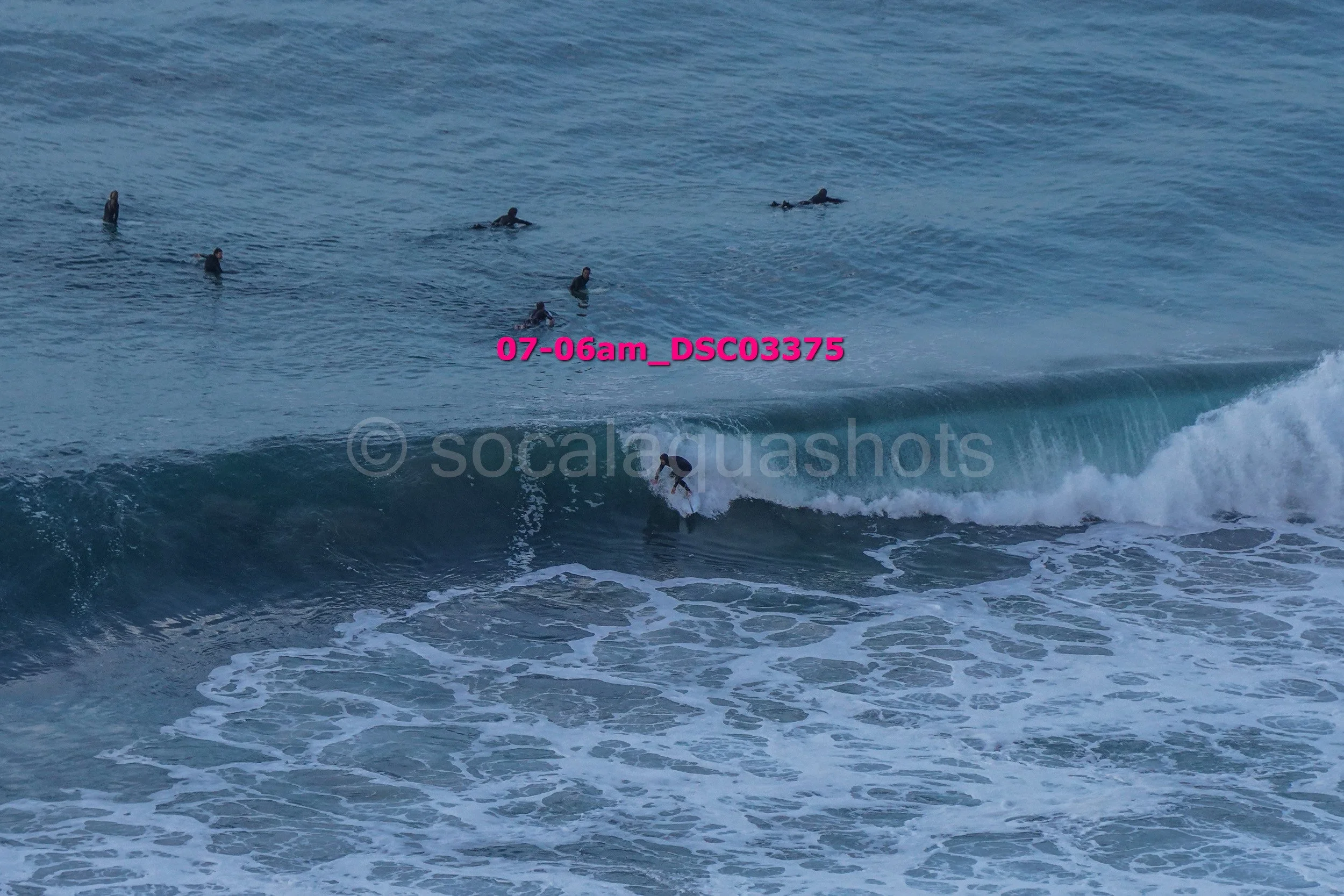 A surfer riding a cresting wave in the ocean with several surfers in the water in the background.