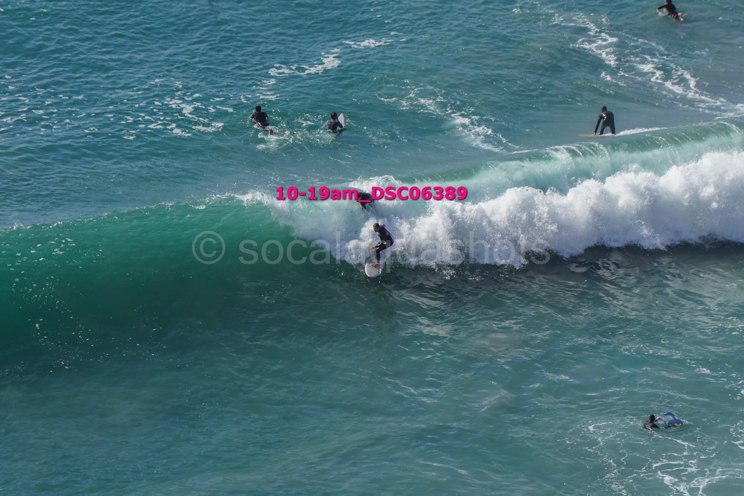 Surfer riding a wave at the beach with several people swimming in the water nearby.