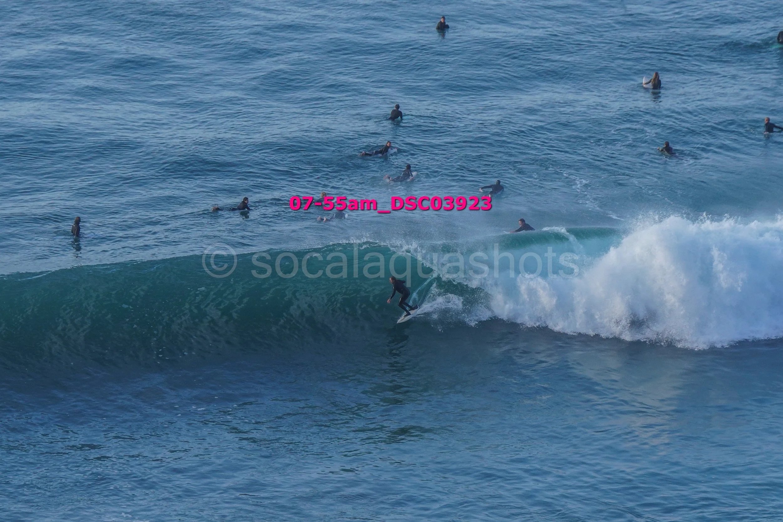 A person surfing on a wave with many people in the water watching in the background.