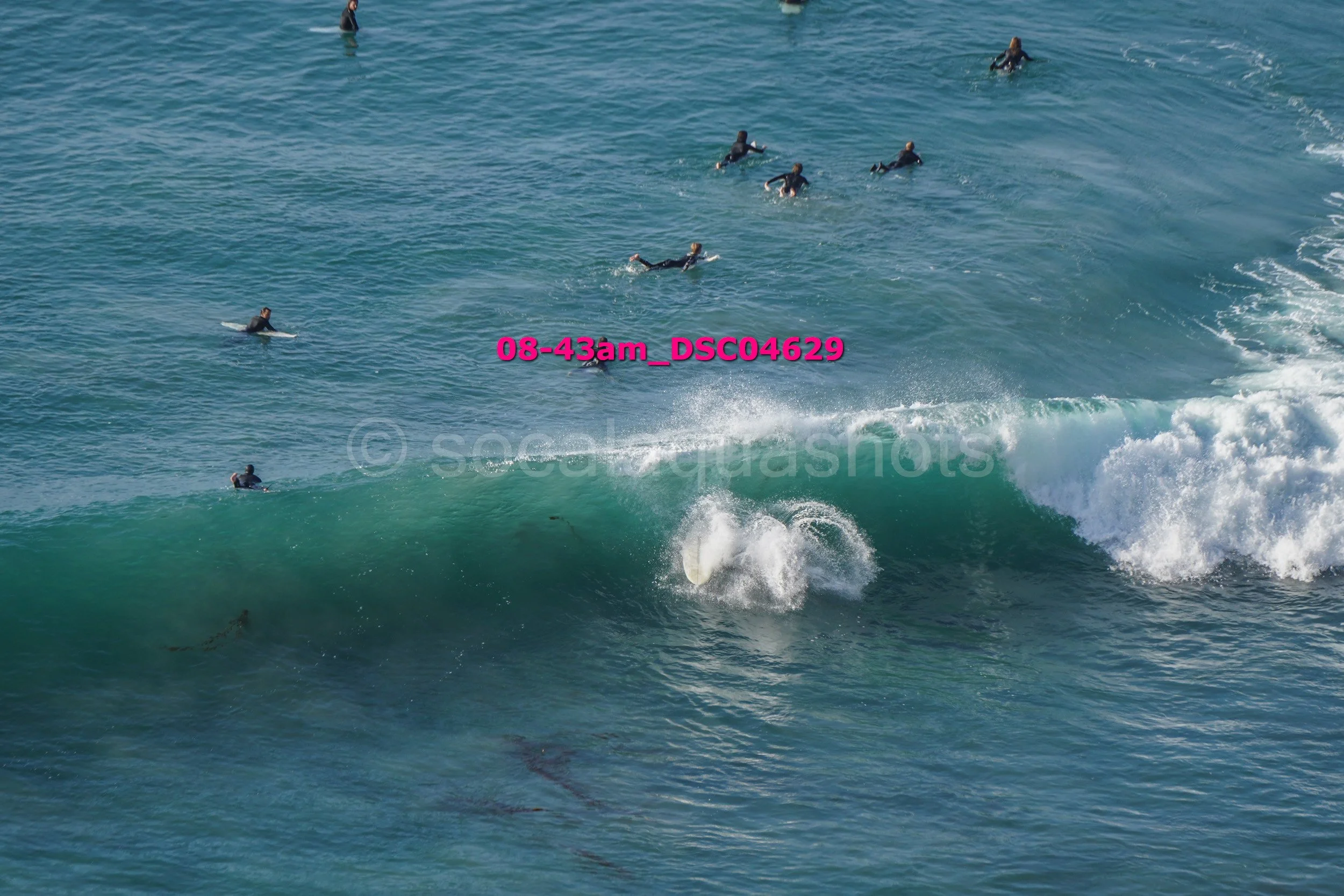 A surfer riding a large wave with several other surfers in the water watching.