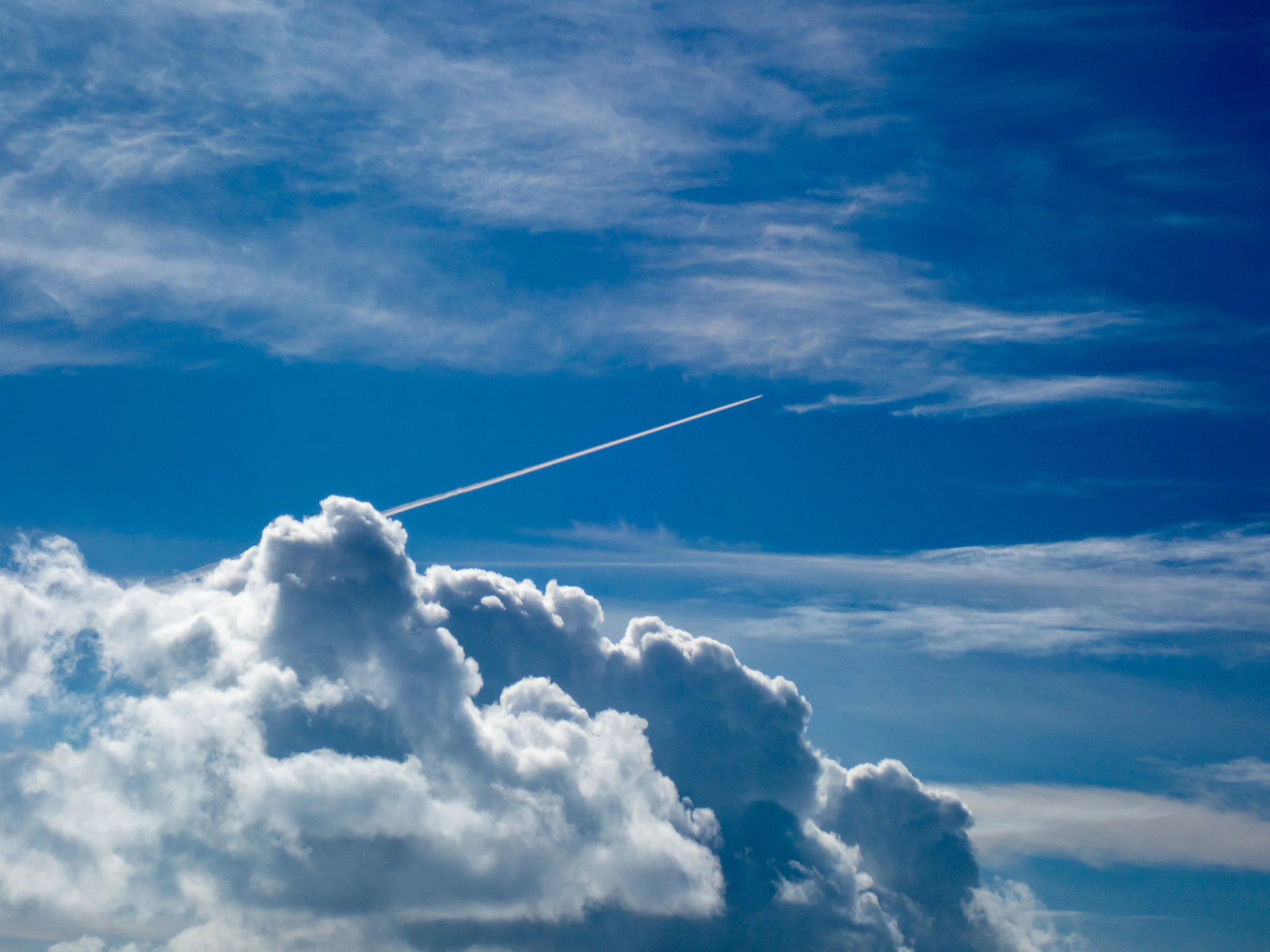 Cloudy blue sky with large clouds and a white jet contrail.