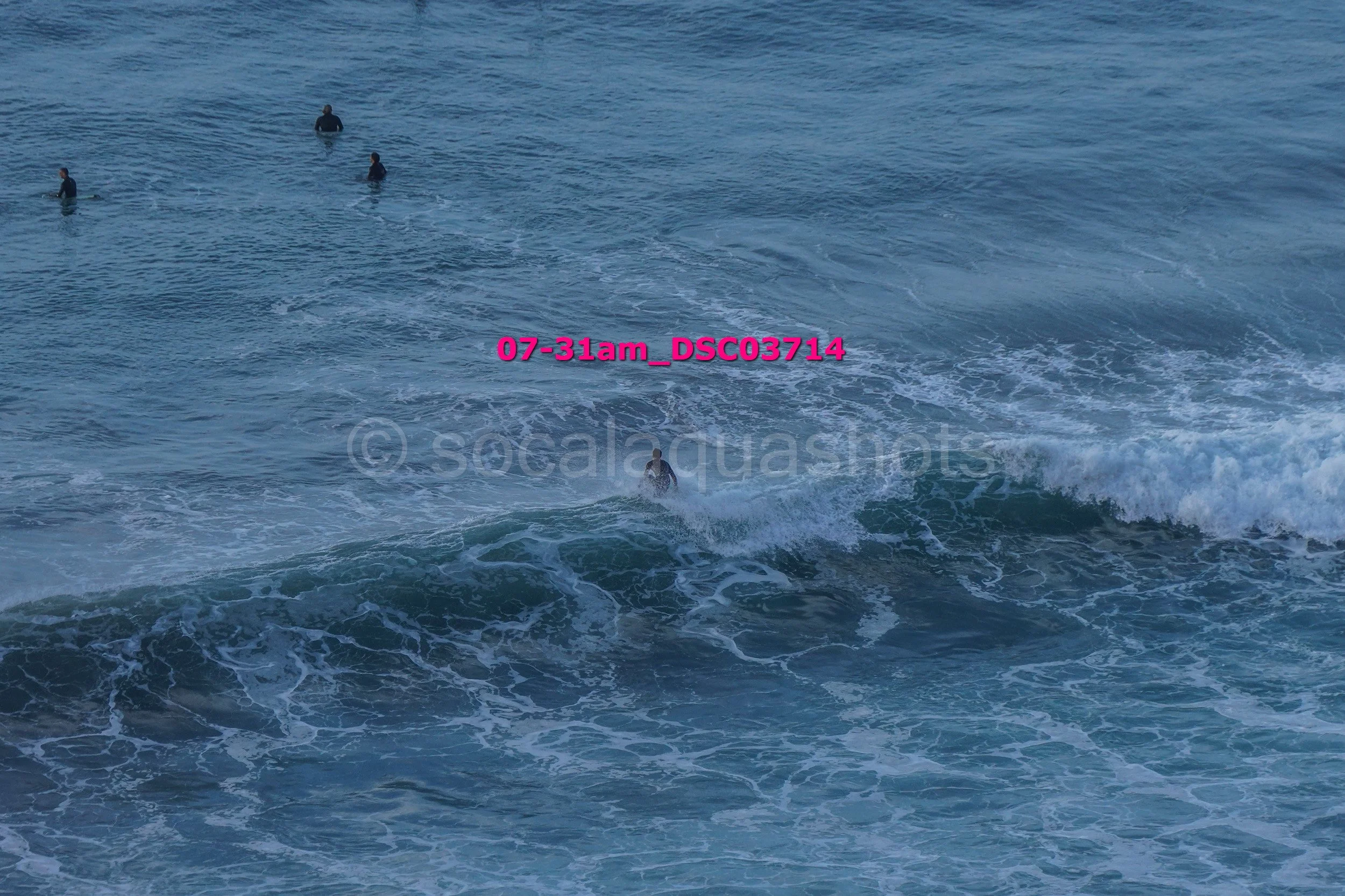 People in the ocean, two near the shore and three further out, some surfing or swimming.