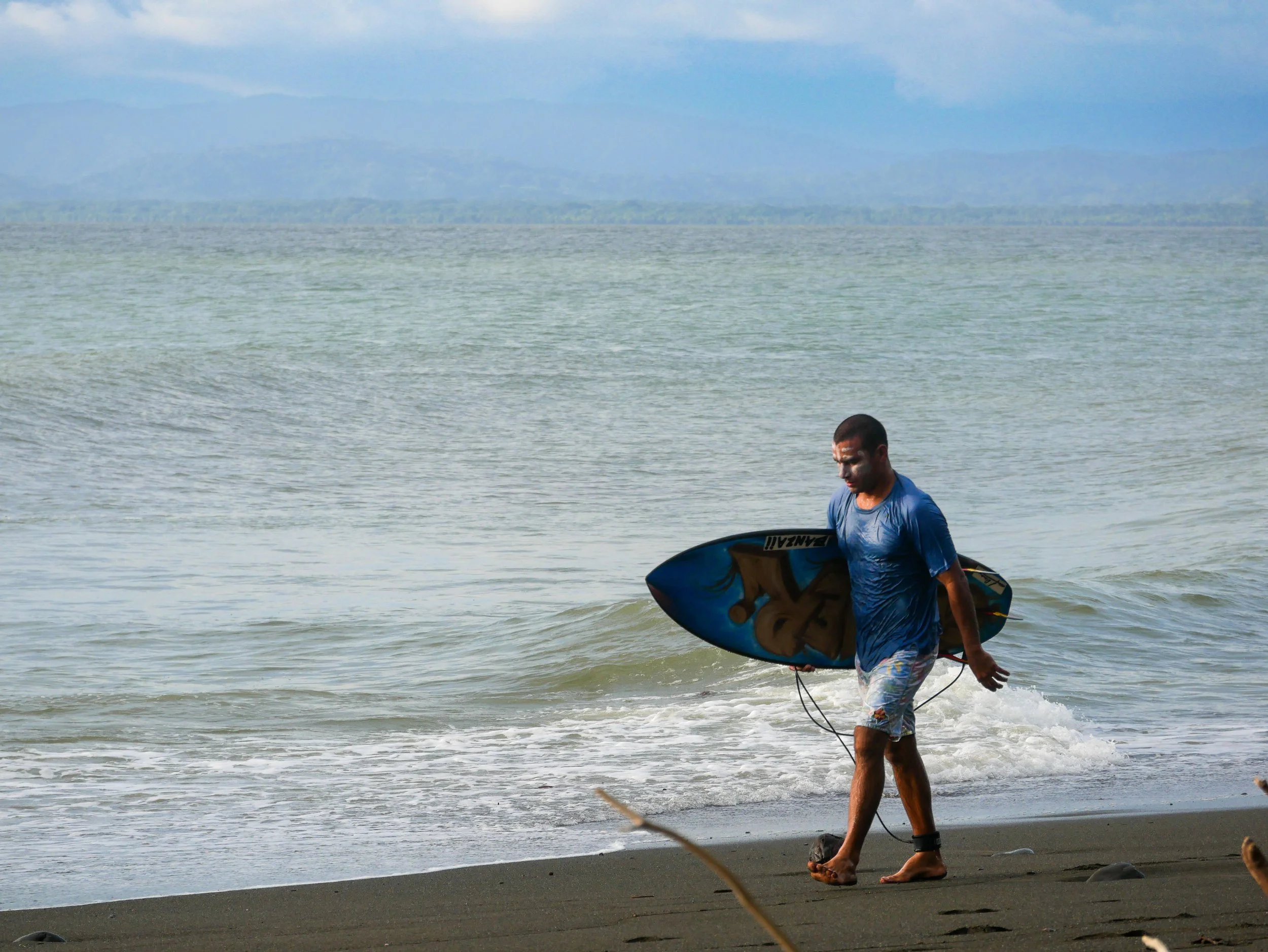 Surfer walking on beach with surfboard, ocean waves in background
