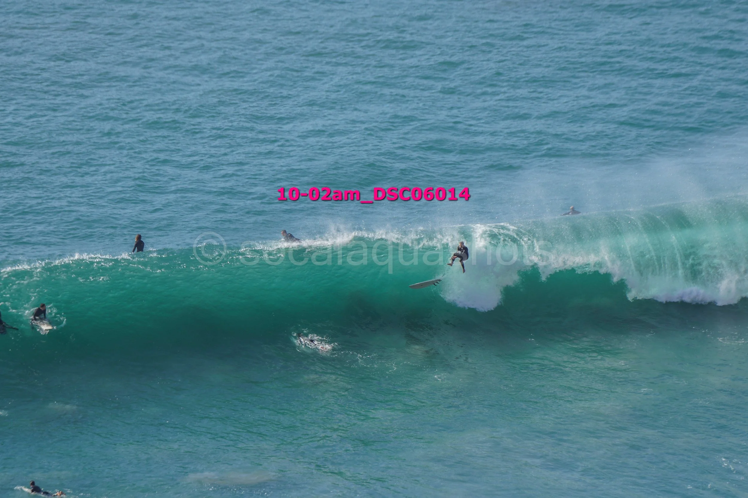 Surfer riding a large wave with other surfers in the water nearby.