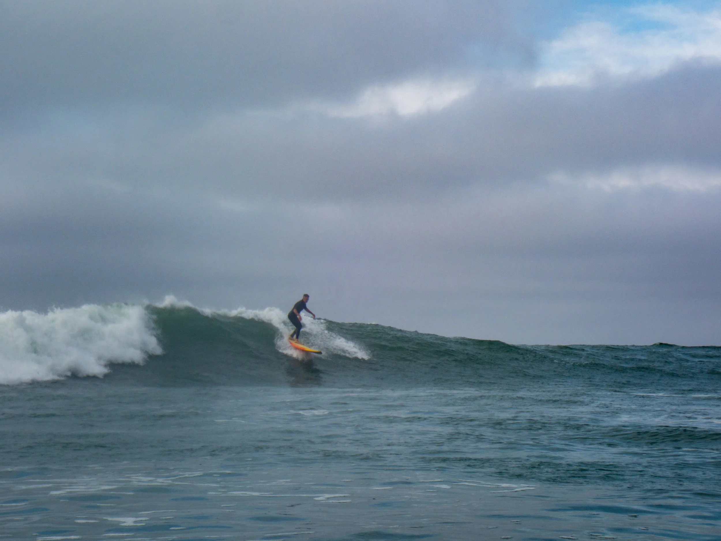 A person surfing on a wave in the ocean under a cloudy sky.