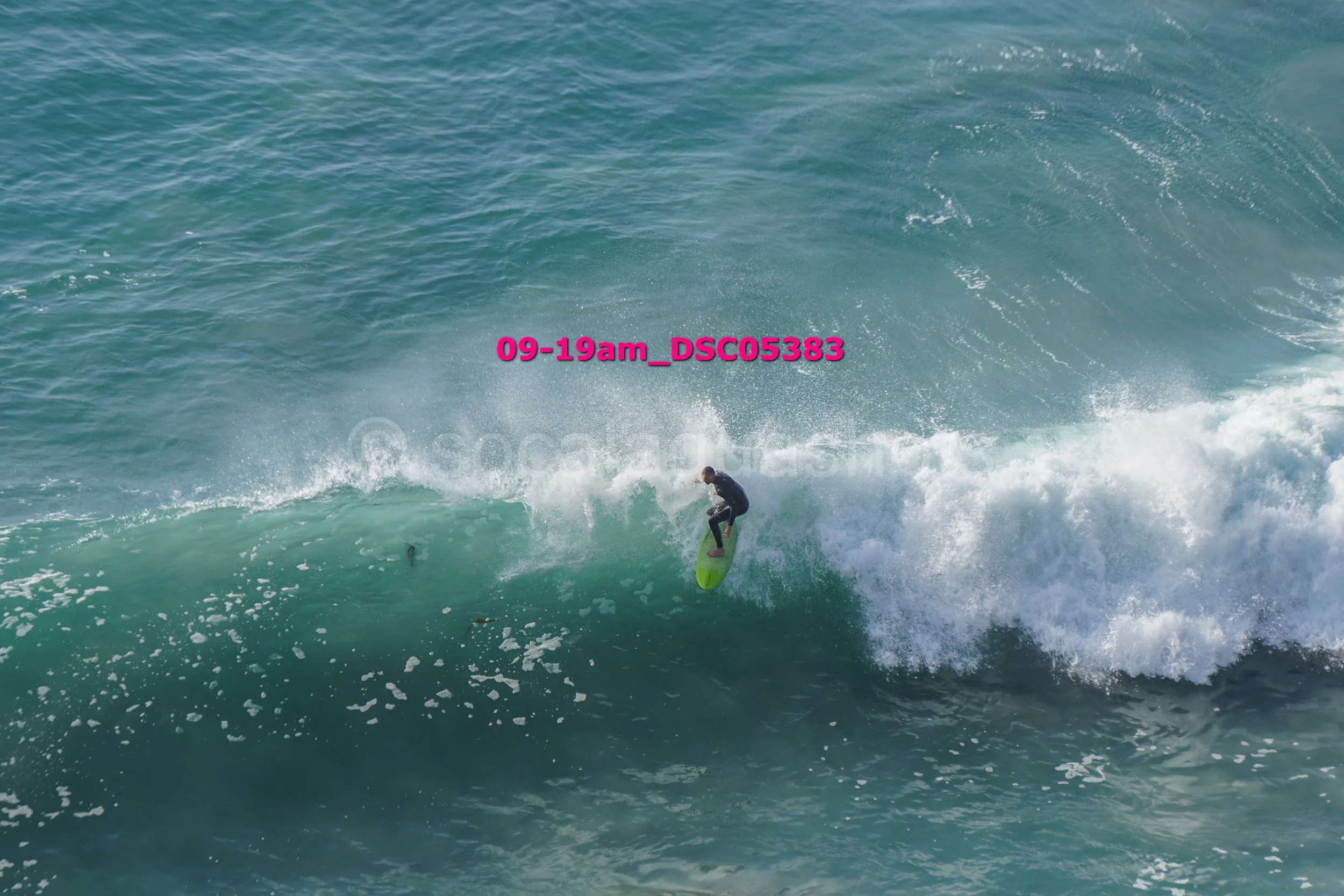 A person surfing on a large ocean wave with white foam, wearing black wetsuit on a green surfboard.