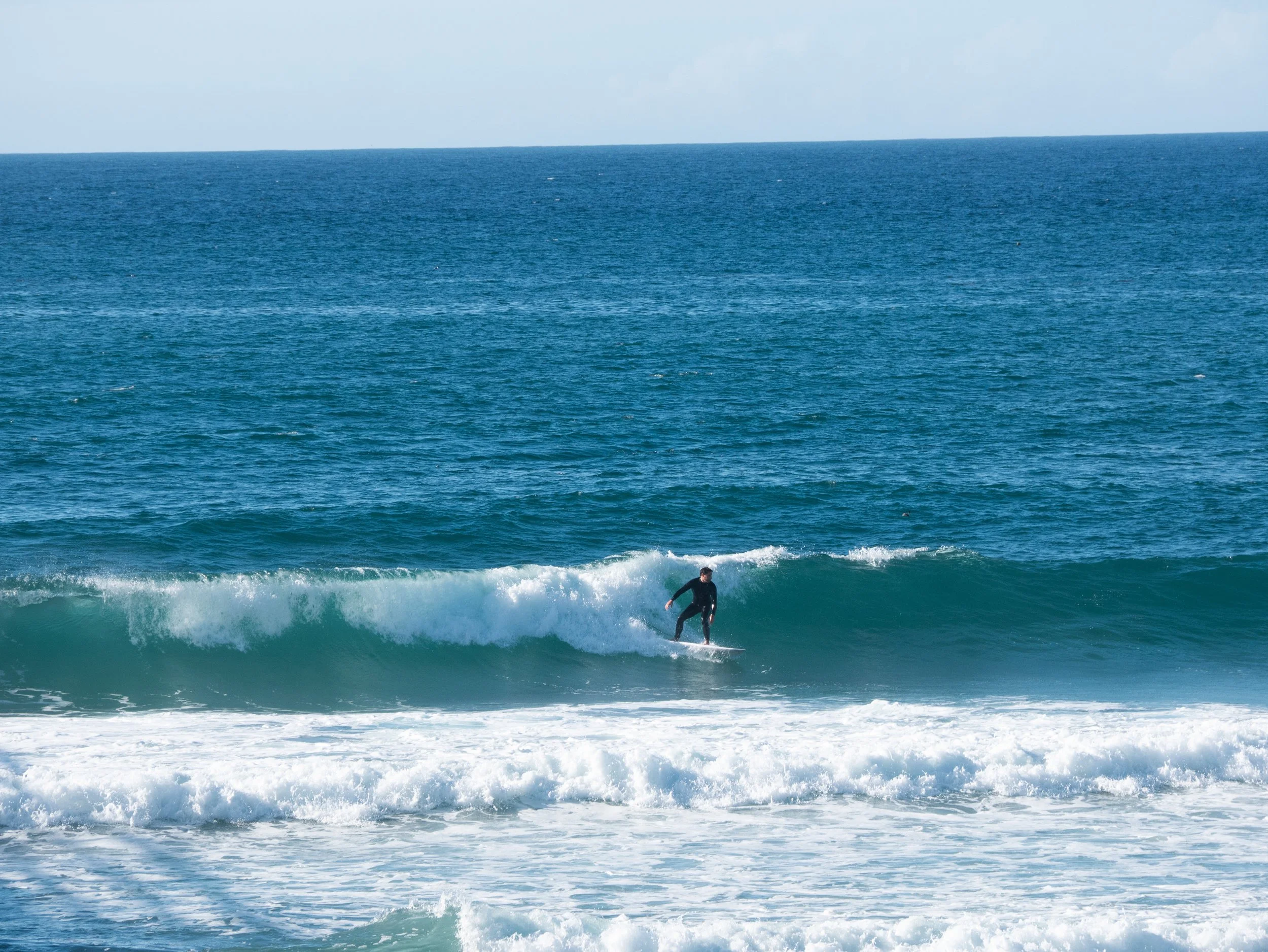 A person surfing on a wave in the ocean with a clear blue sky overhead.