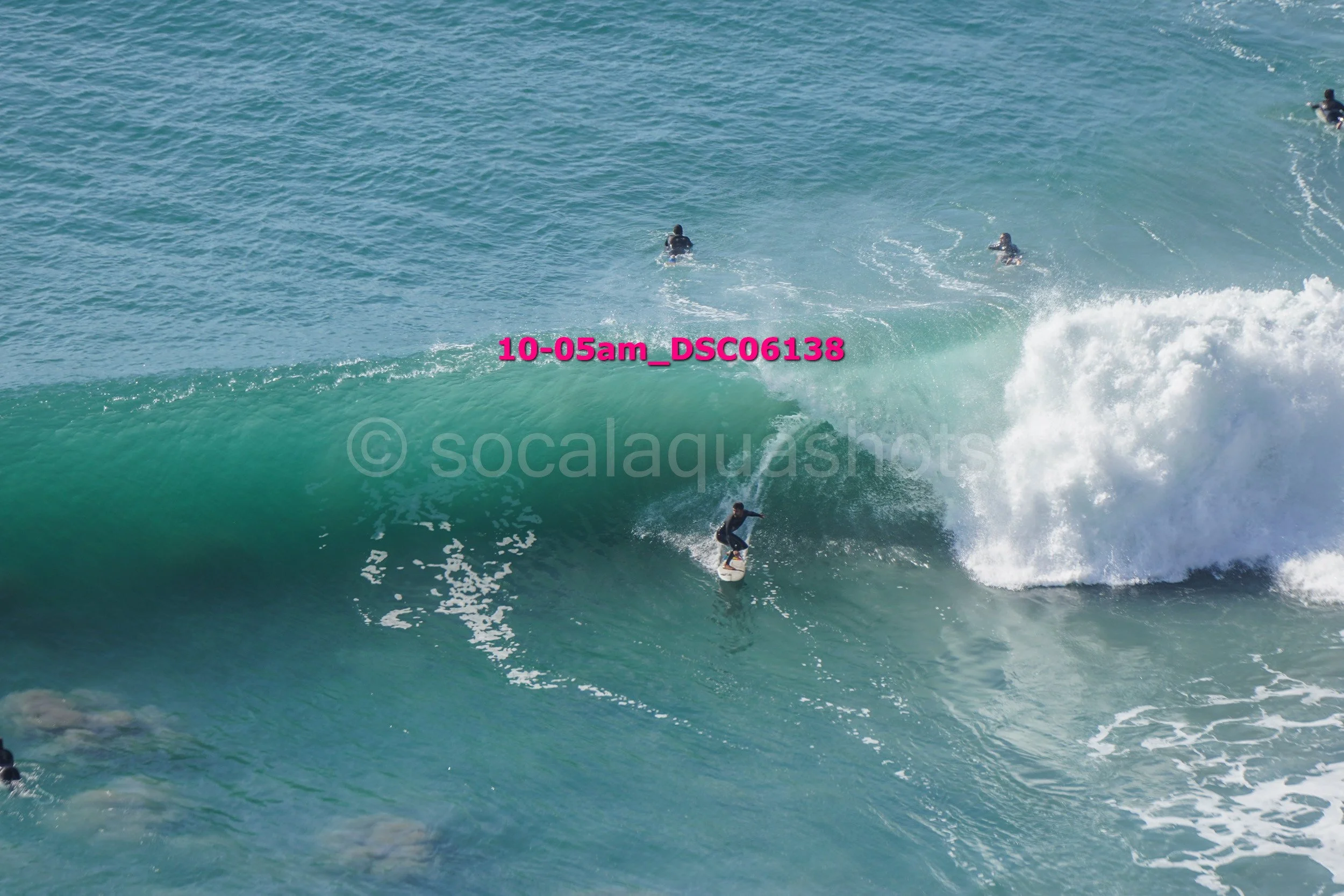 Surfer riding a wave with two other surfers in the background in the ocean.