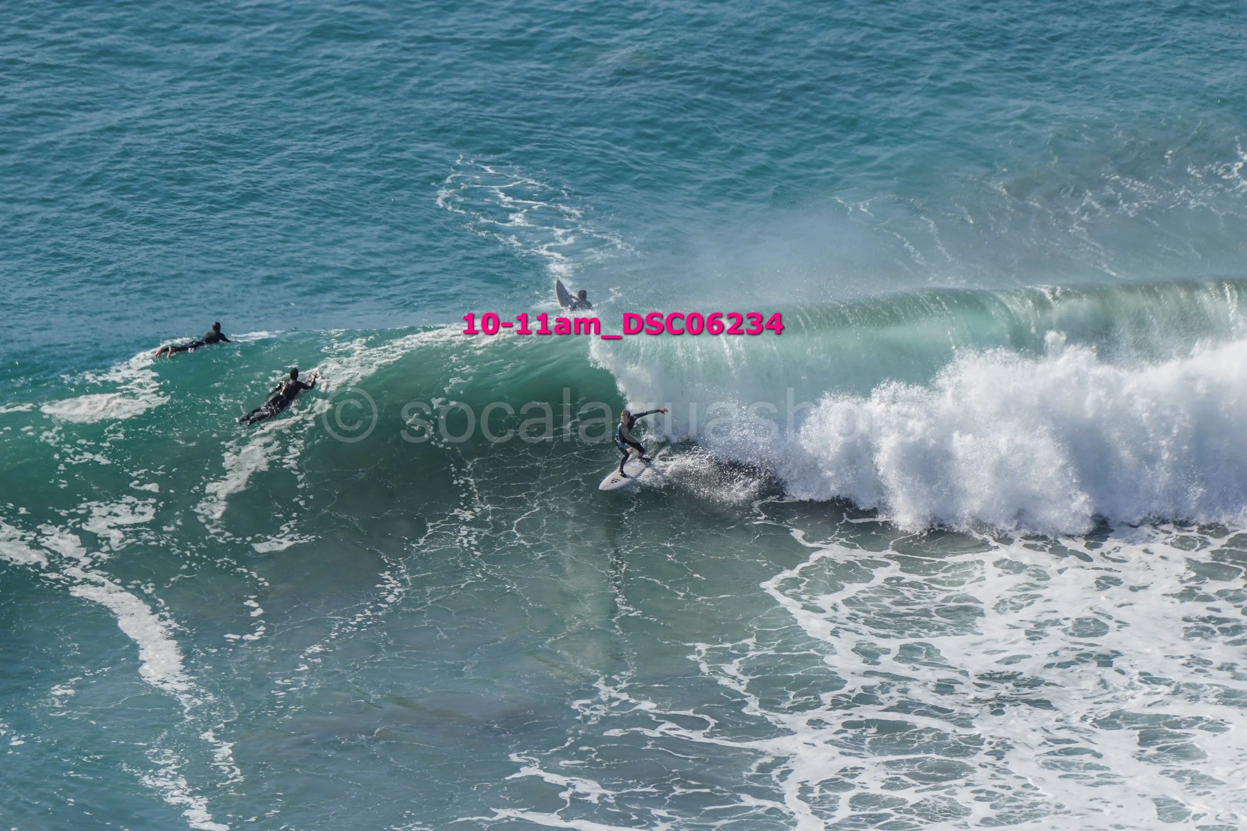 A surfer riding a large wave while three others are paddling nearby in the ocean.