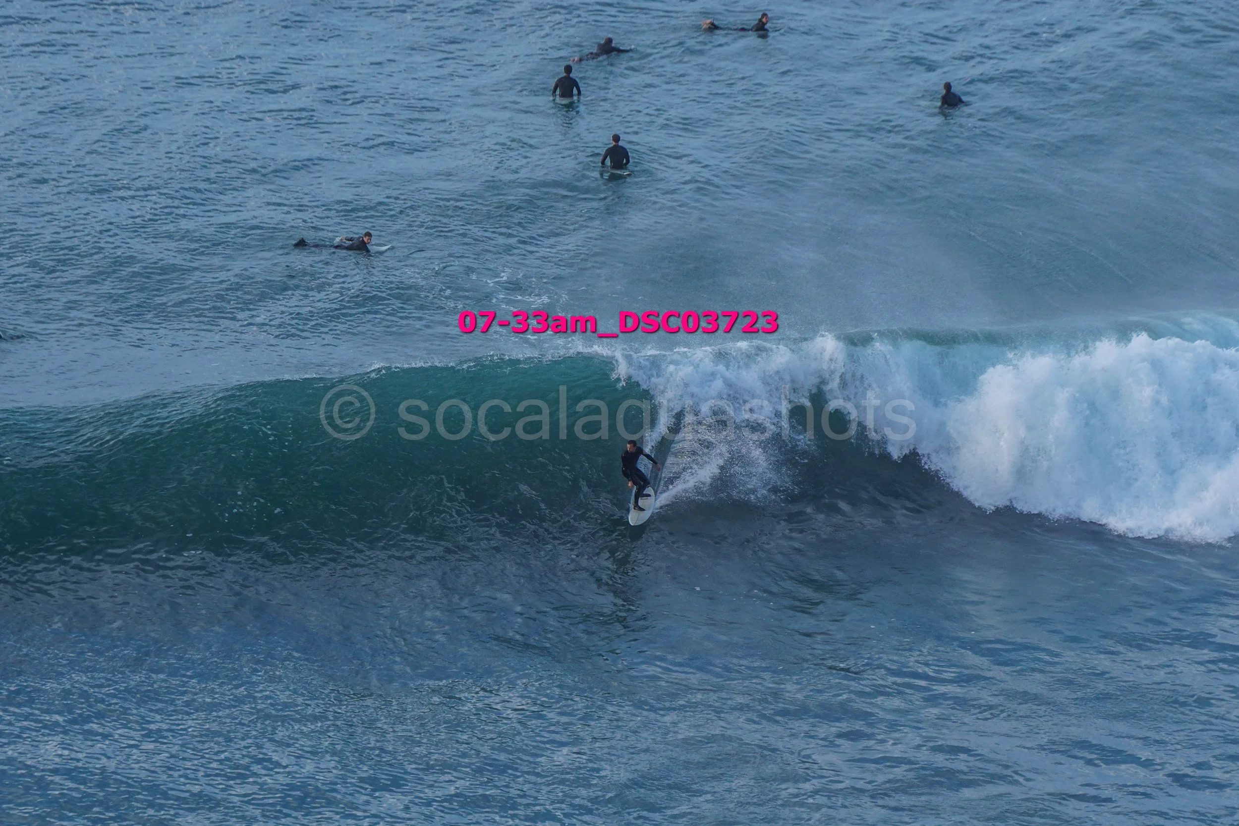 A person surfing on a wave with other surfers floating in the water nearby.