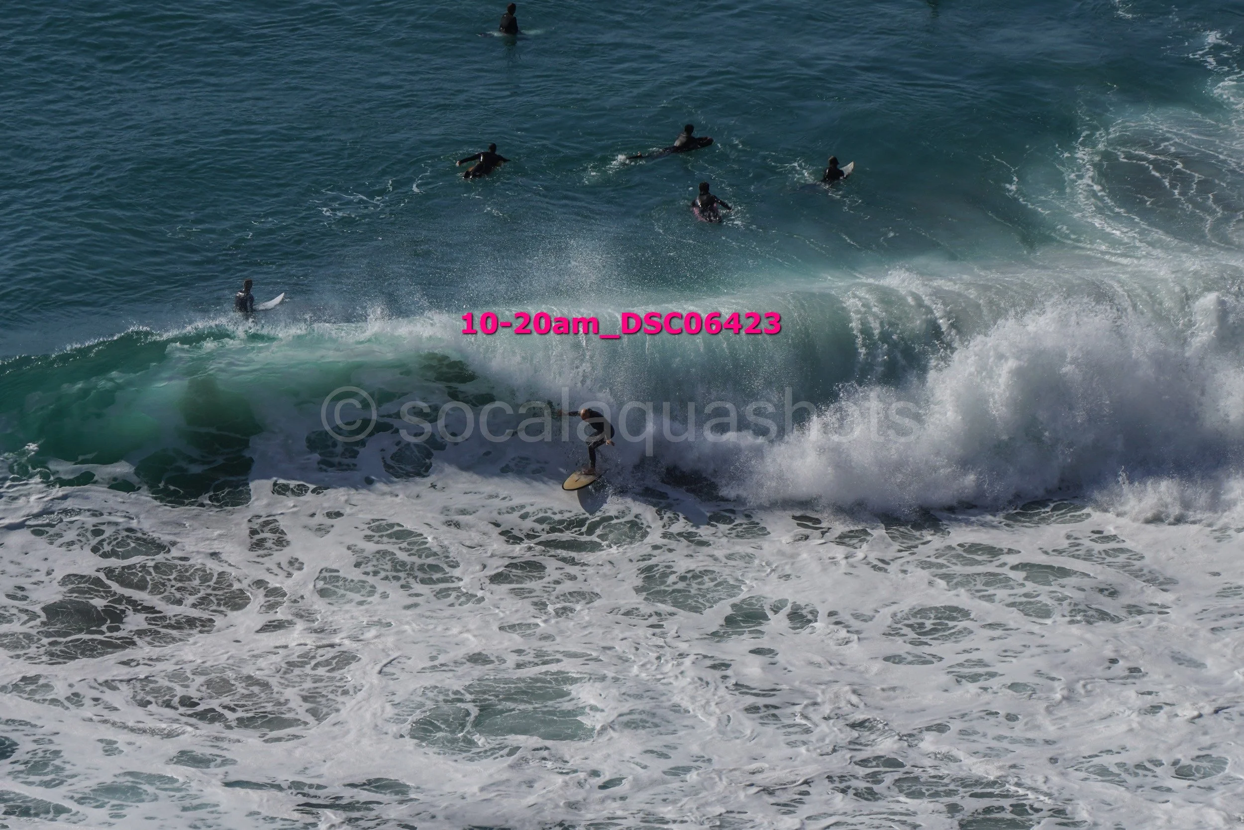 Surfers riding and waiting for waves in the ocean, with foam and spray from the breaking waves.