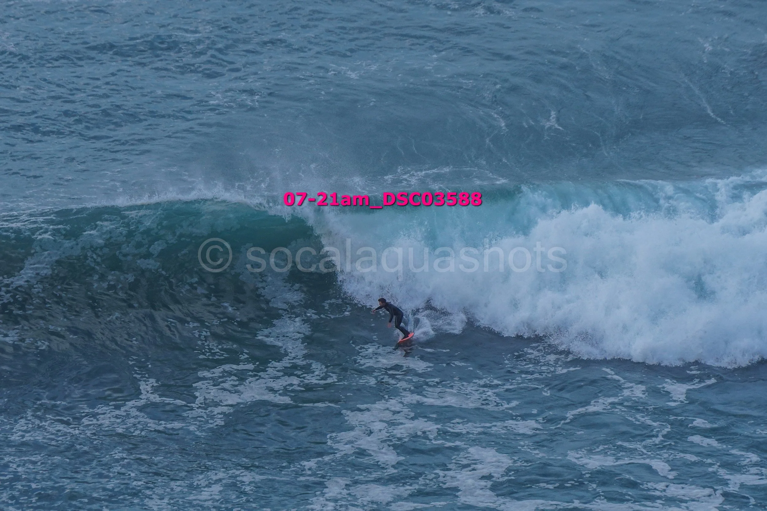 A surfer riding a wave in the ocean during daylight with a watermark and timestamp overlay.
