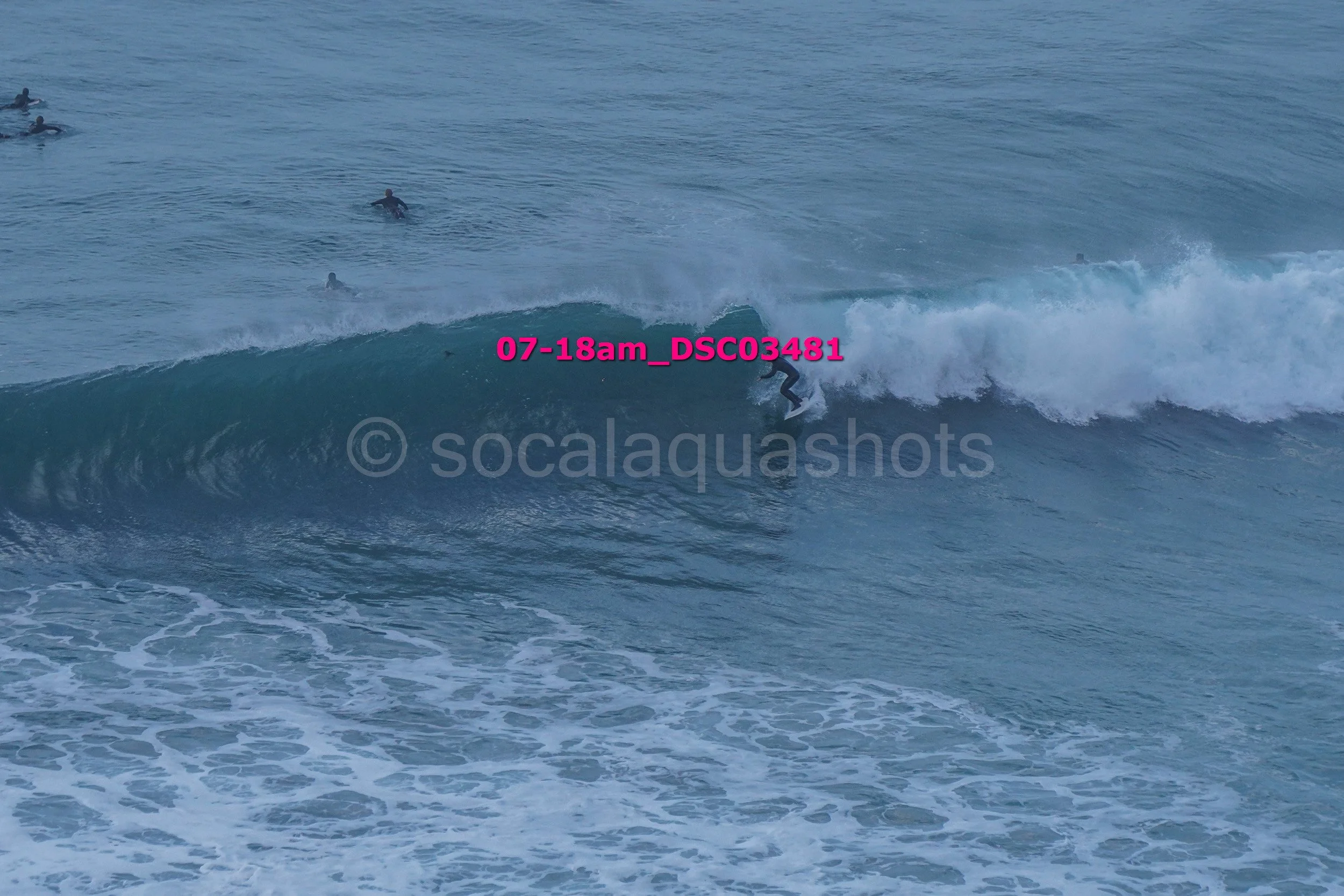 A person surfing a wave in the ocean with several others in the water nearby.