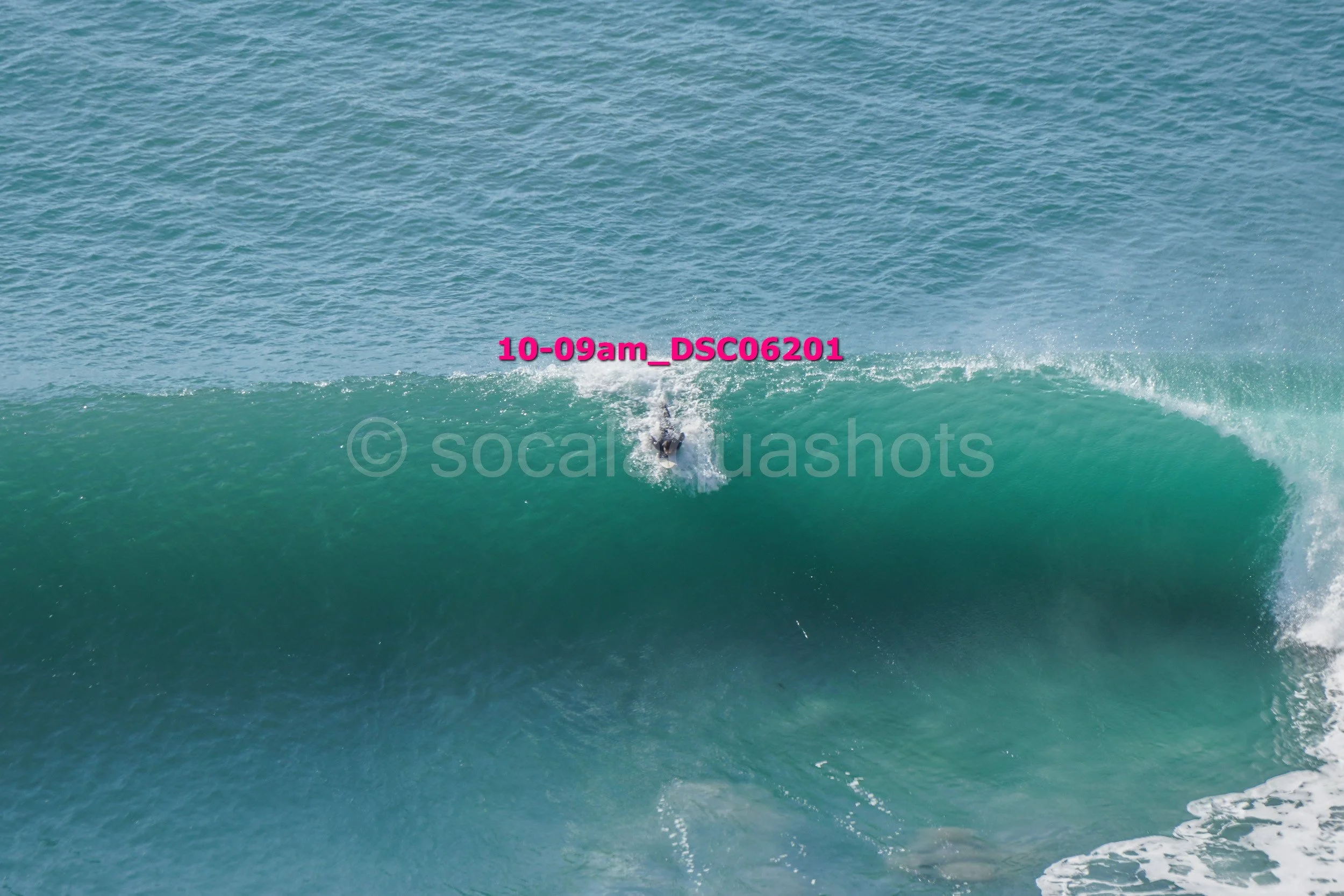 A person surfing on a large ocean wave with visible water spray, riding the crest of the wave.
