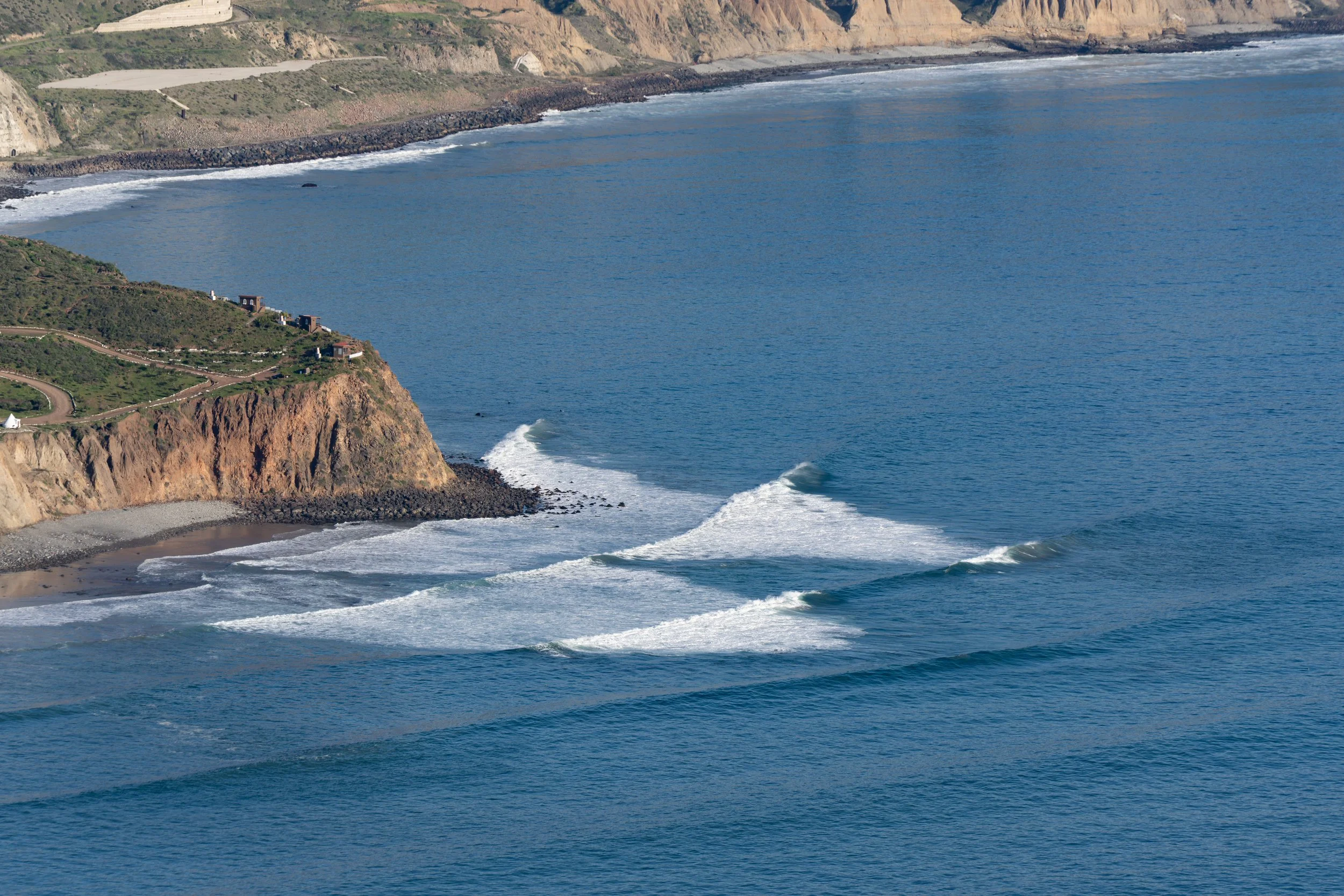 Cliffside coastline with waves crashing against the shore and small houses along the edge of the land.