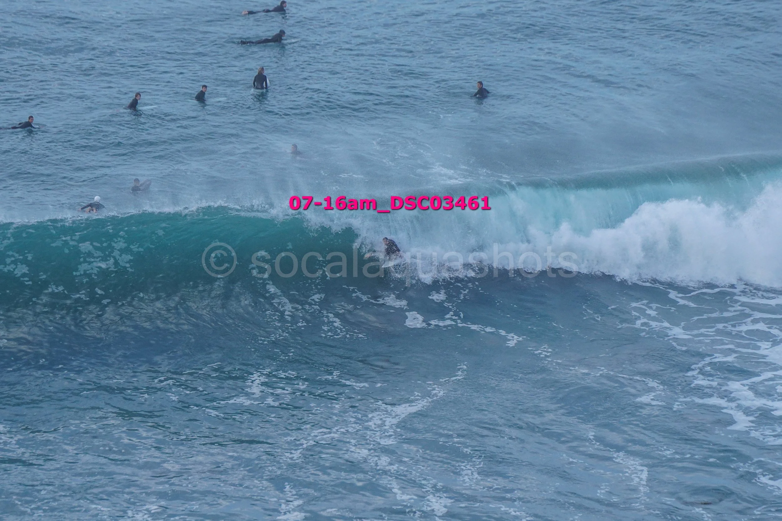 A person surfing on a wave in the ocean with multiple other surfers in the water nearby.