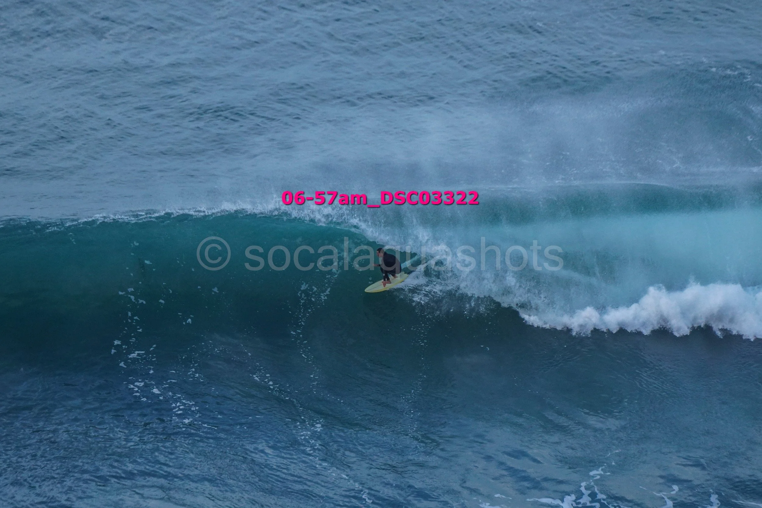 A person surfing on a wave in the ocean, with the view of a large wave curling over the surfer.