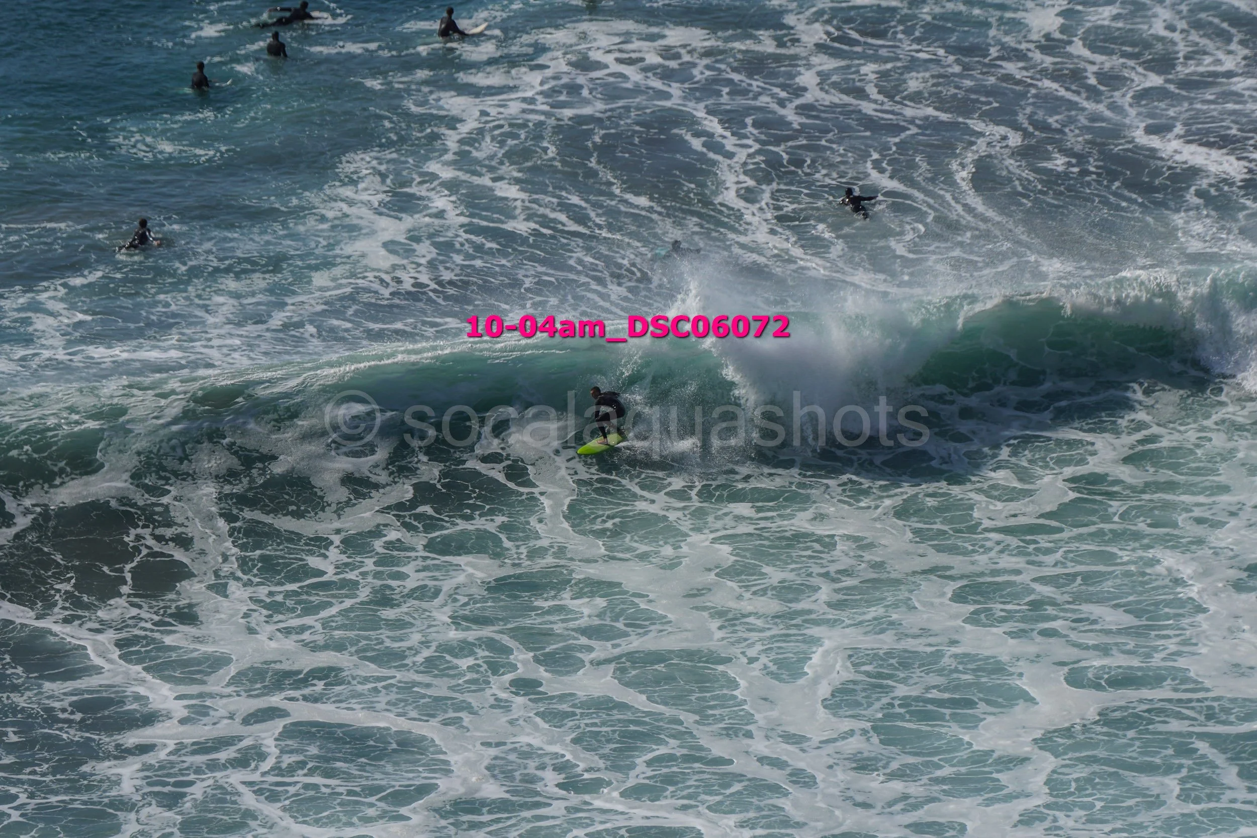 A person surfing on a wave in the ocean with several other people swimming nearby.