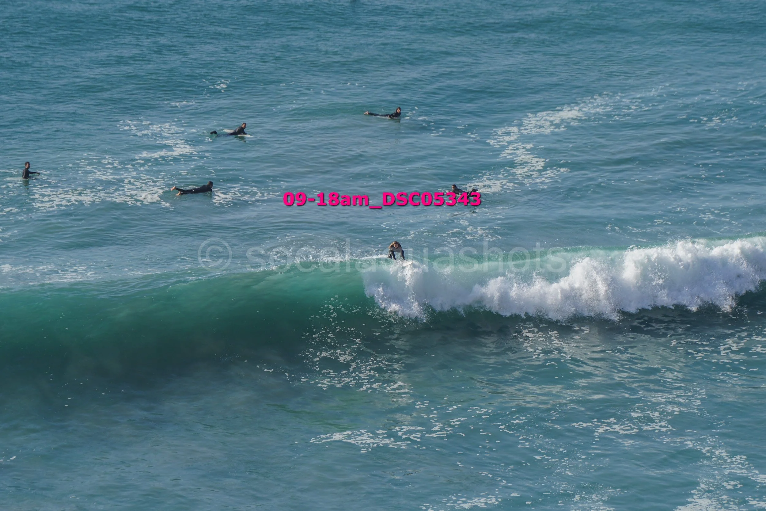 Surfer riding a wave with several swimmers in the background in the ocean.