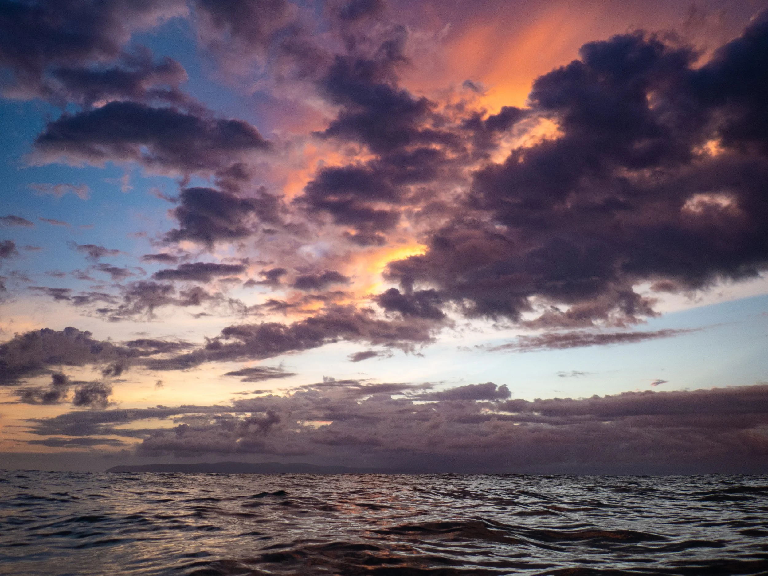 Dark clouds in the sky at sunset over a body of water.