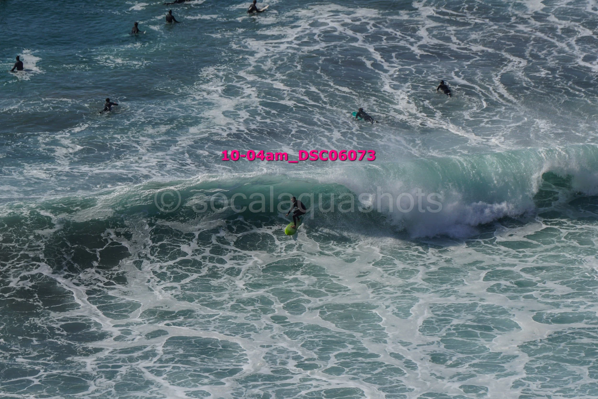 Surfer riding a wave with several other surfers in the water nearby.