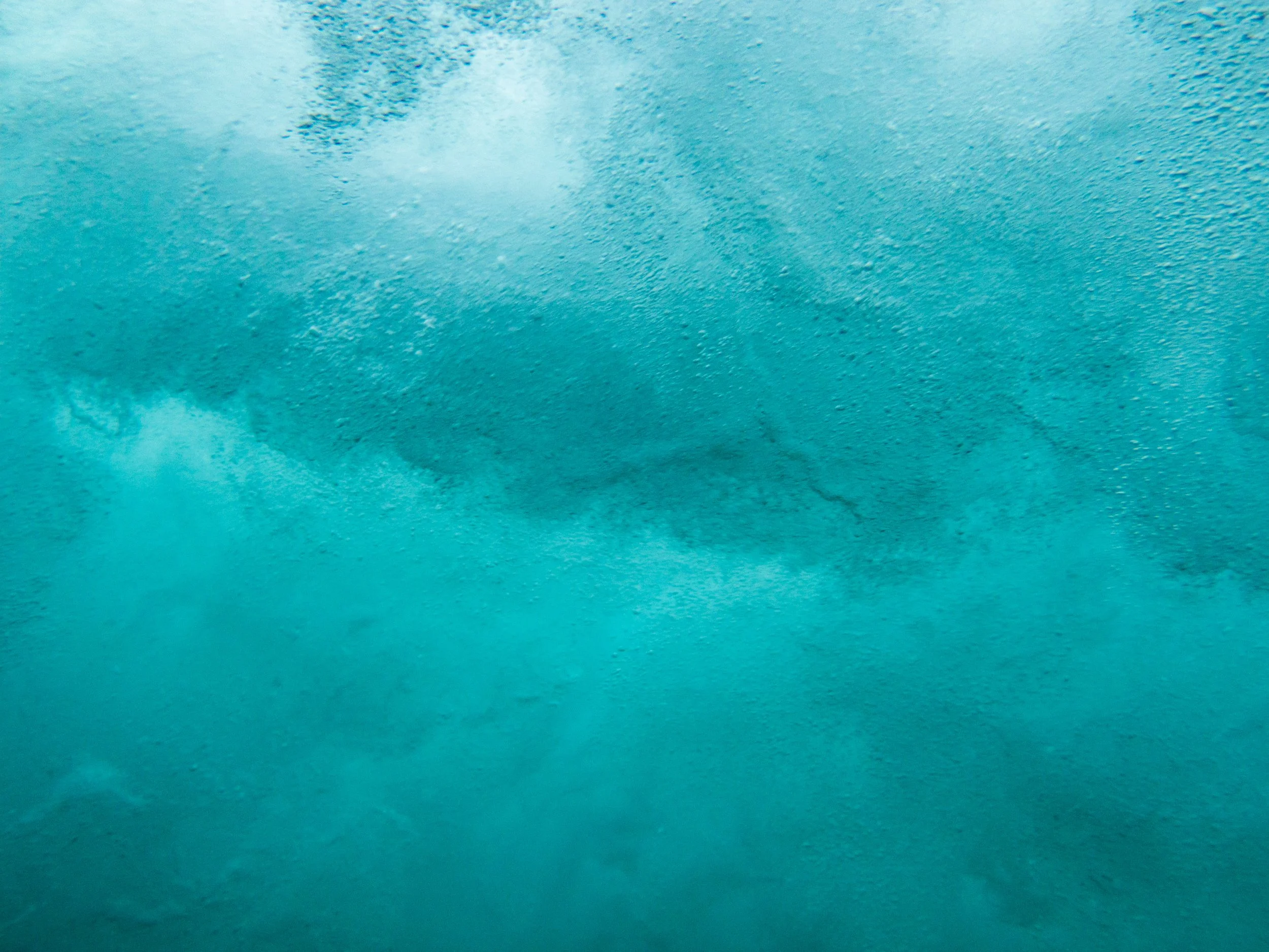 Underwater view of a blue wave with foam and bubbles.