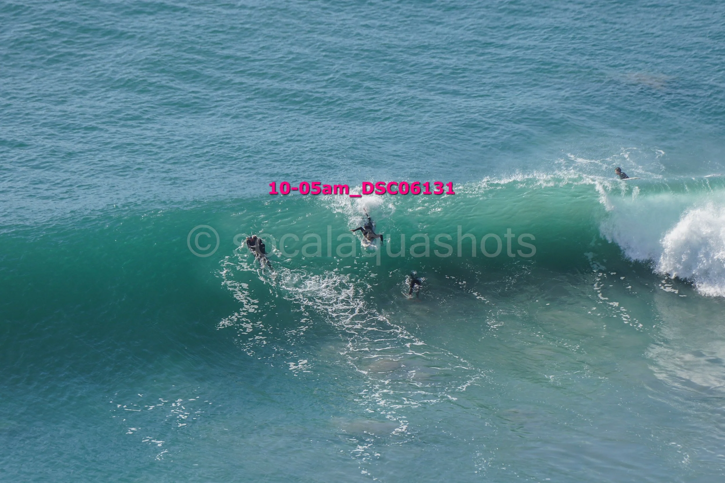 Group of surfers riding a large ocean wave, with some standing and some falling.